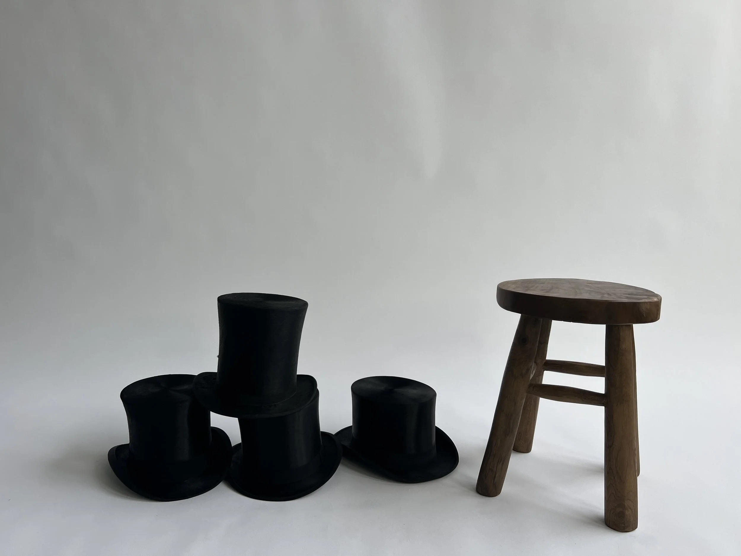 The image shows a minimalistic setting with two chairs placed against a plain, light gray background. The chair on the left is black and has a modern, curved design. The chair on the right is made of natural wood with a rounded seat and four sturdy l
