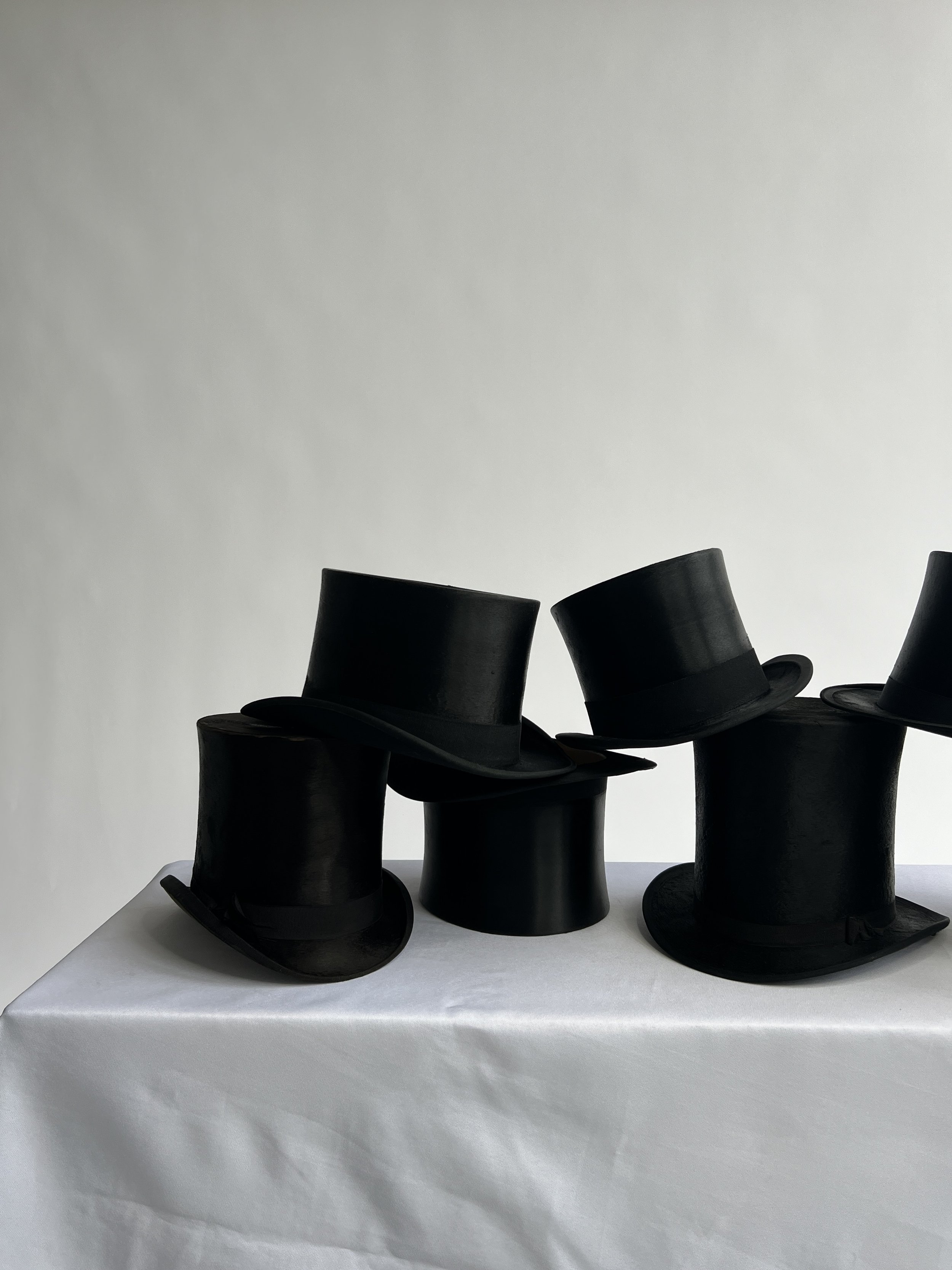 A group of black top hats in a luxury pile on a white surface with a plain white background.