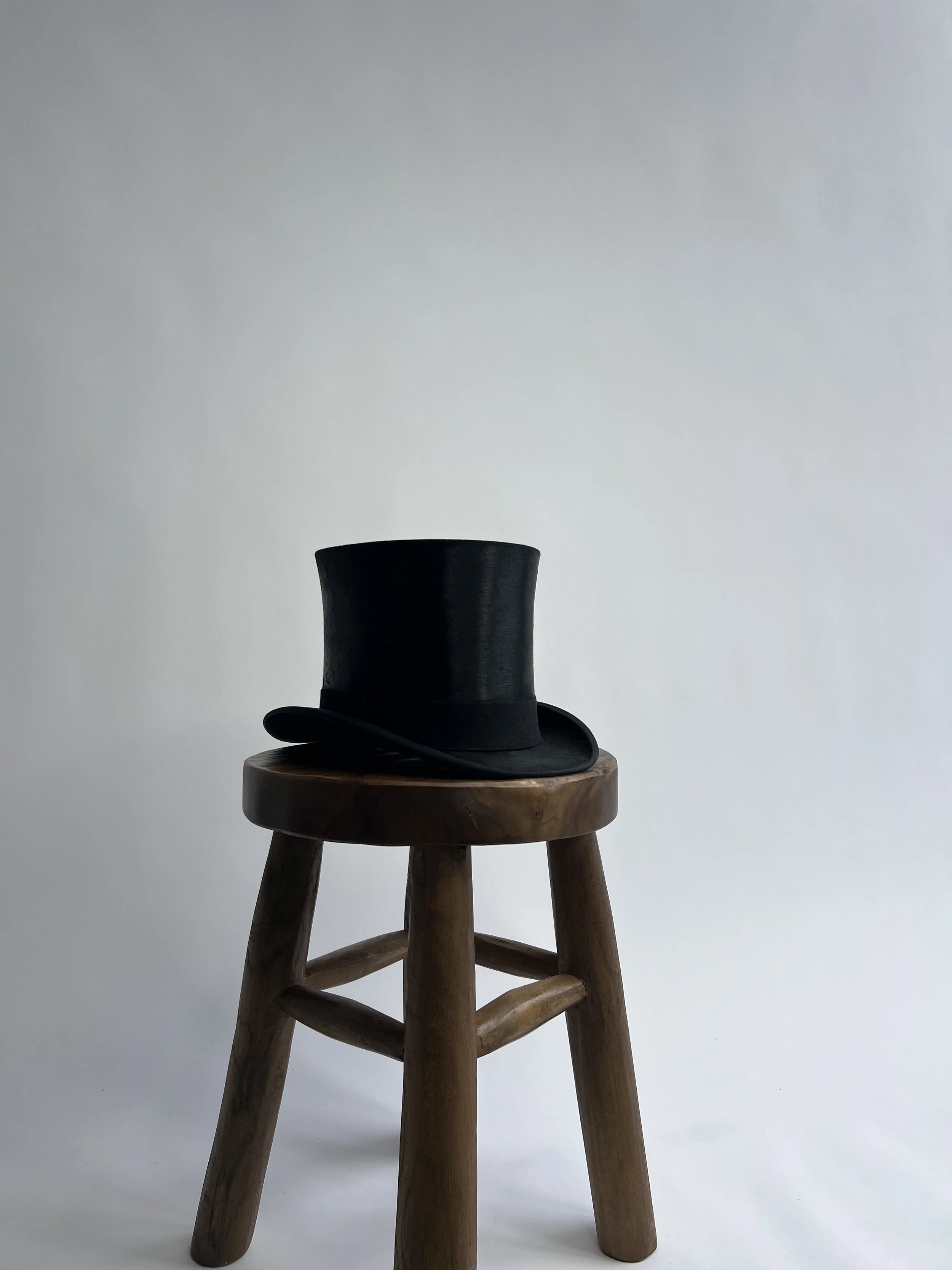 A black top hat and a bow tie are placed on a small round wooden table against a plain light gray background.