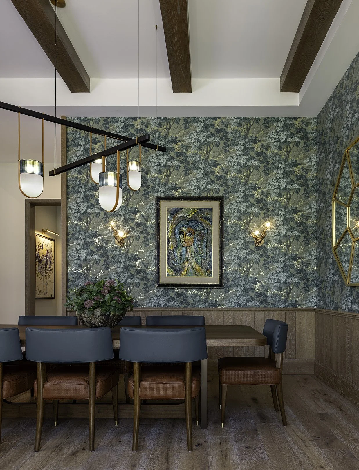 A dining area with a wall decorated with green leafy wallpaper, a framed portrait of a woman, two wall-mounted sconces, a modern chandelier, a wooden table, teal chairs, and a large potted plant.