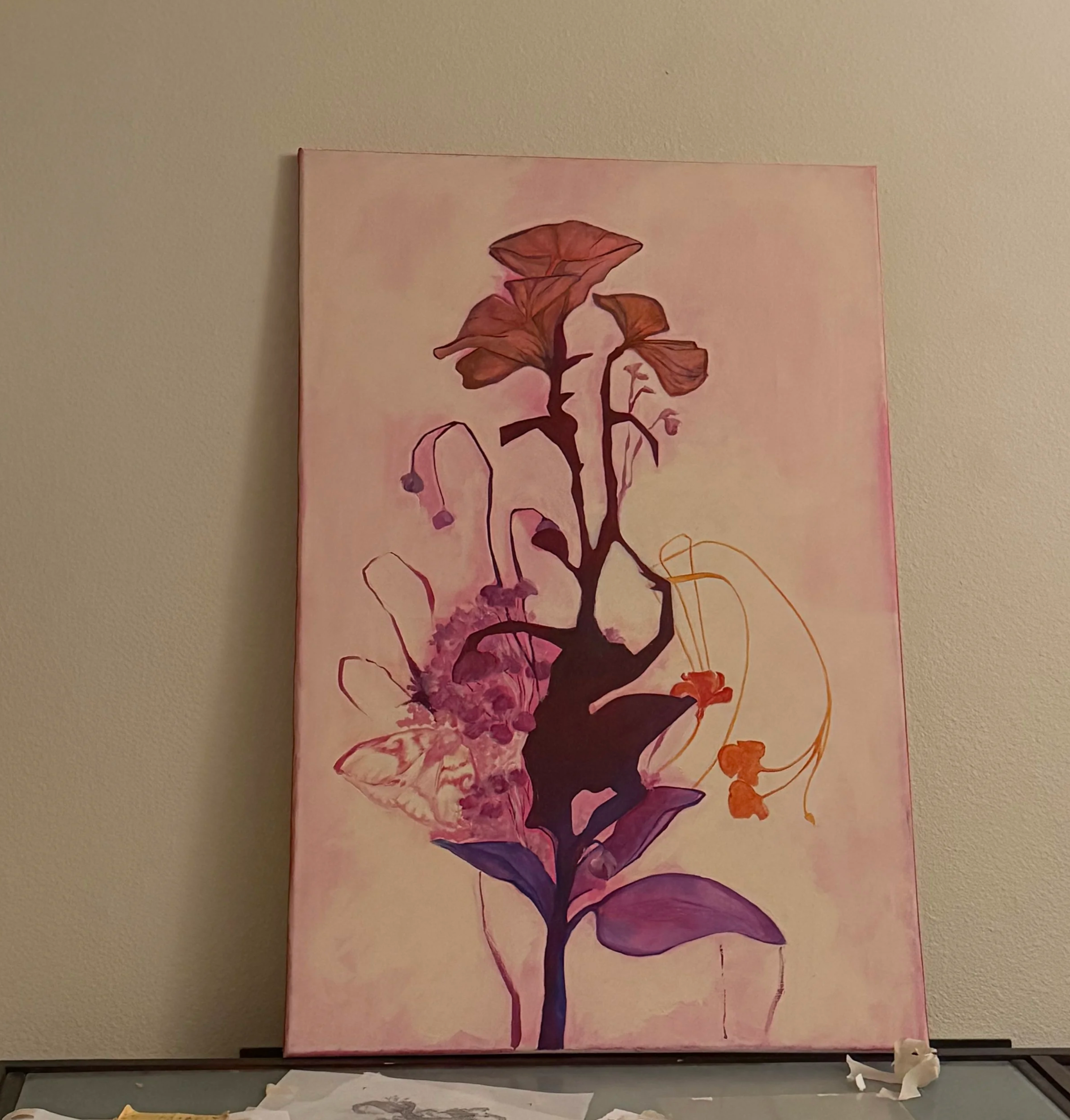 A colorful painting of a flower with orange, purple, and pink hues hanging on a beige wall in an art studio. 