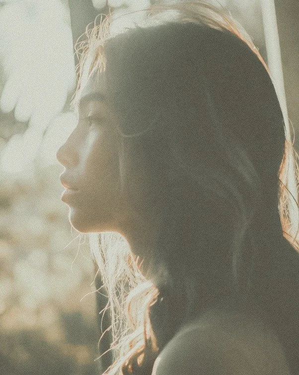Profile of a woman with long hair looking at a window with sunlight.