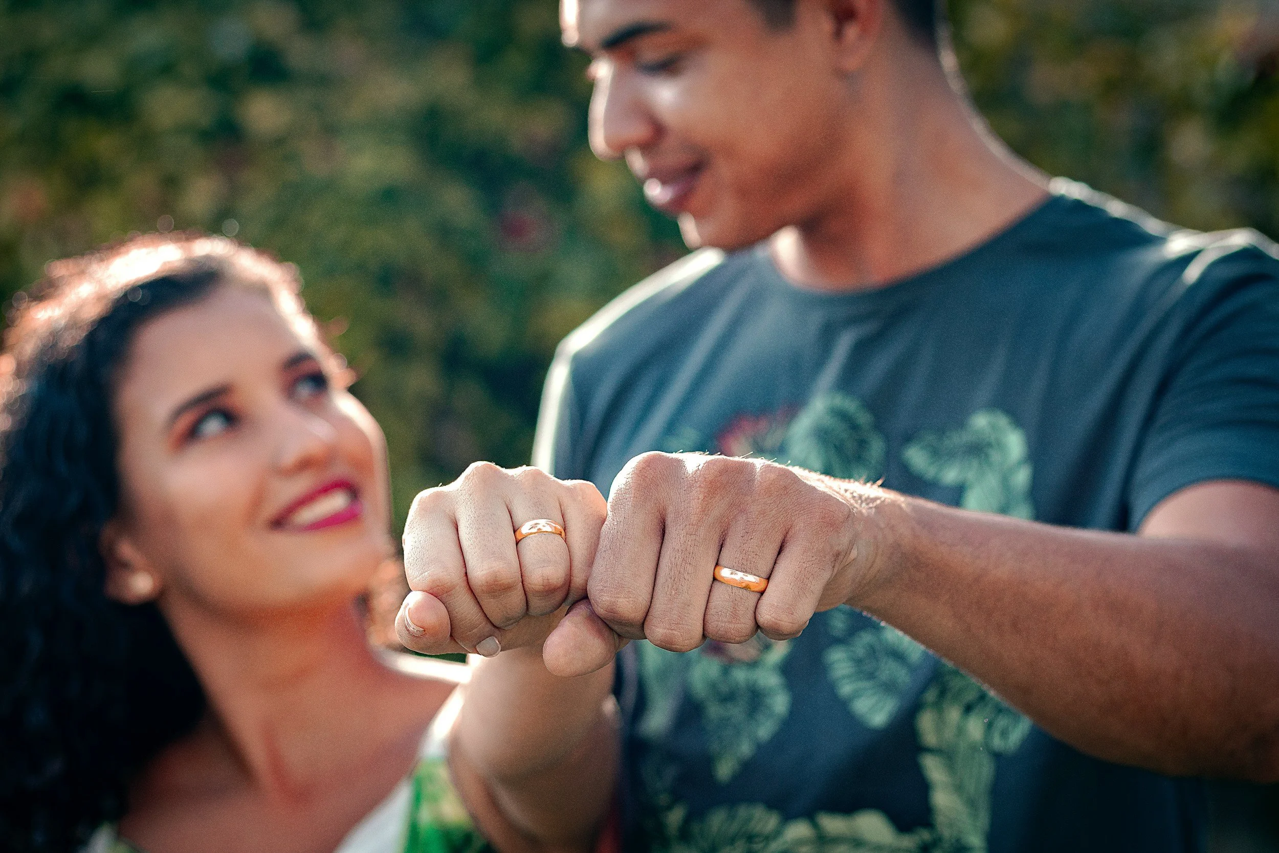 A couple showing their wedding rings, touching fists and looking at each other outdoors.