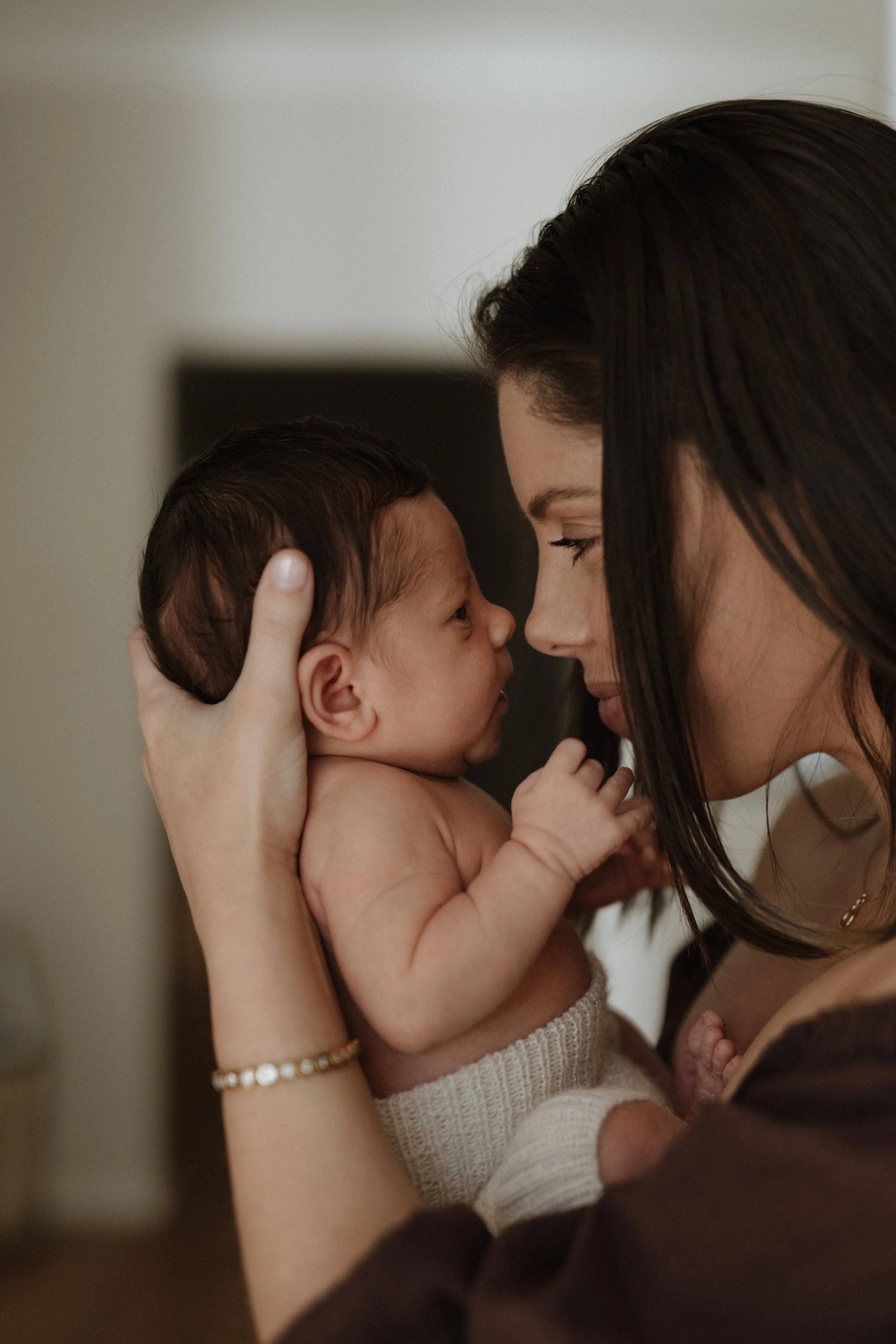 A woman holding a newborn baby close to her face, touching foreheads and gazing into each other's eyes
