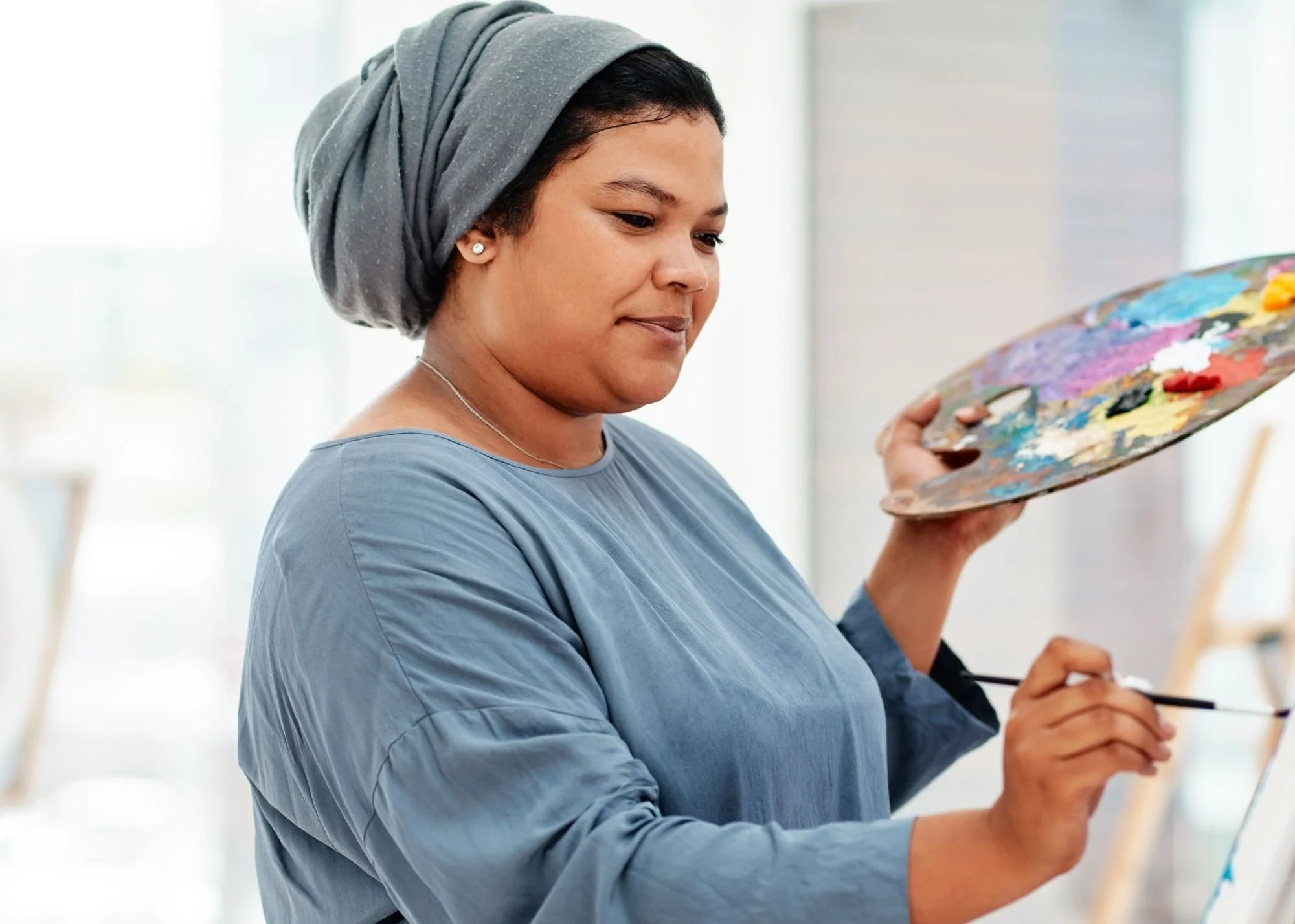 A woman in a blue top and head wrap paints as part of our arts programs for mental health and wellness