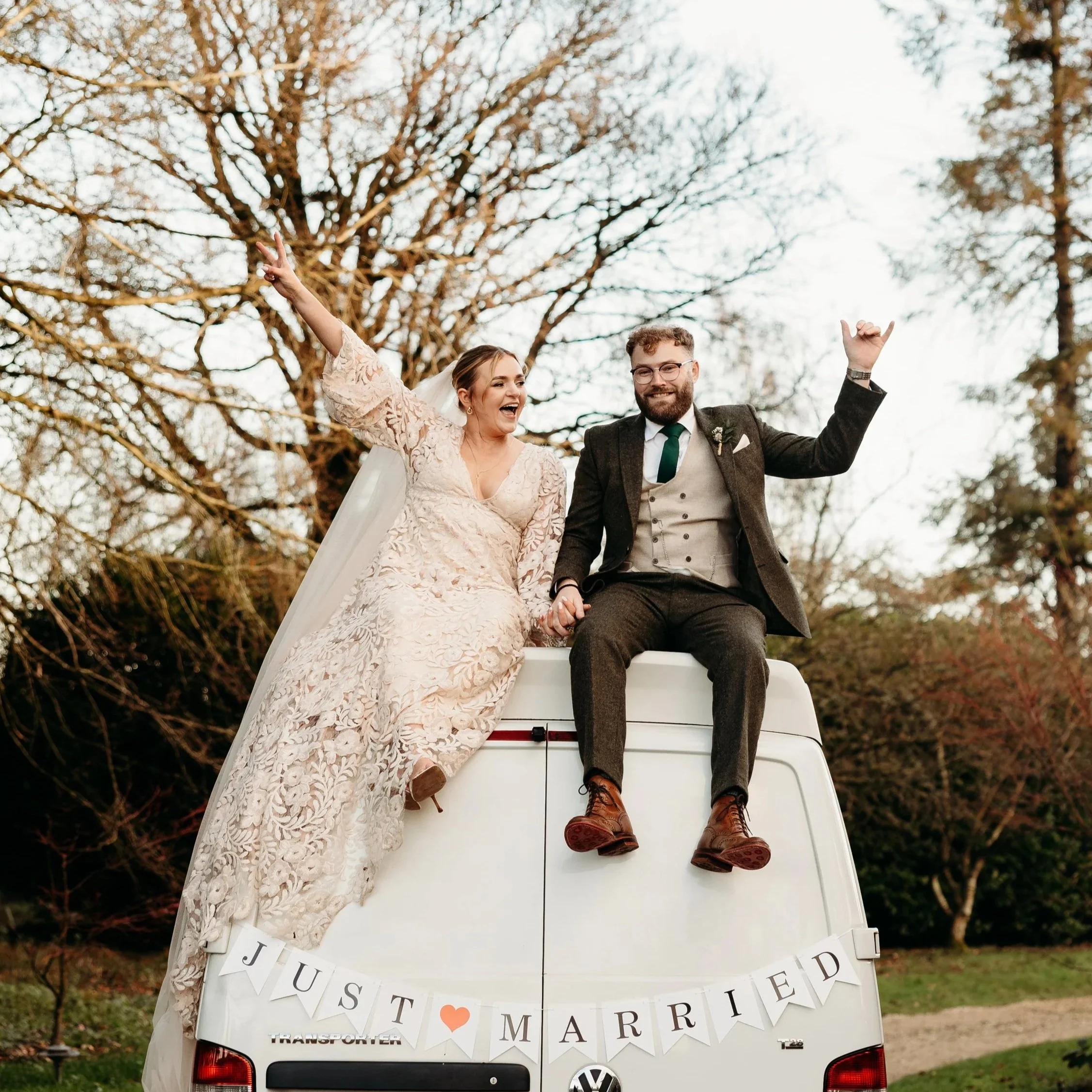 Newly married couple sitting on top of a van with wedding decorations, holding hands, and celebrating outdoors at Matara Centre, Cotswolds, Gloucestershire. An image that shows the couples' personality.