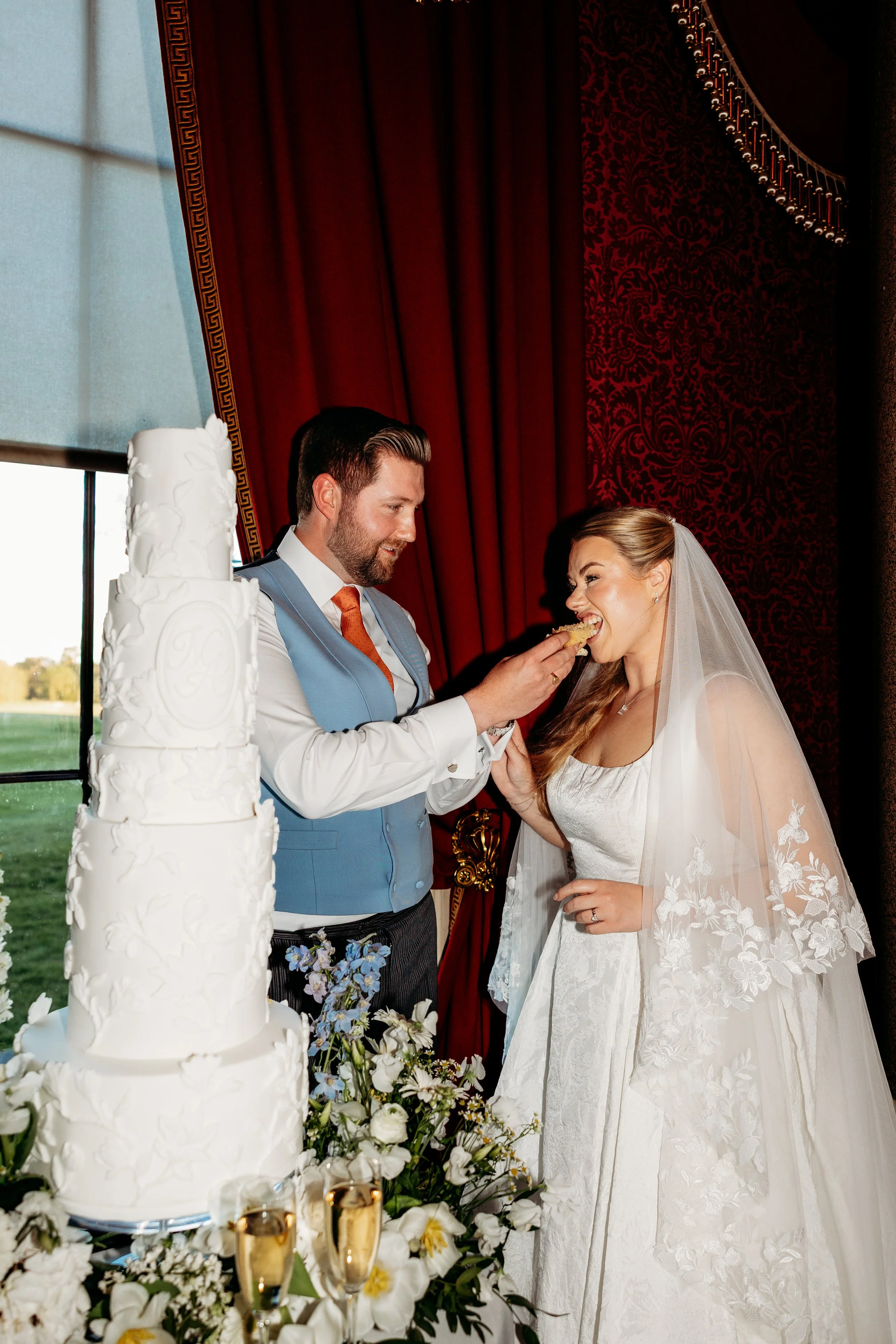 A bride and groom at their wedding reception, with the groom feeding the bride a piece of wedding cake at Goodwood Estate, Sussex.