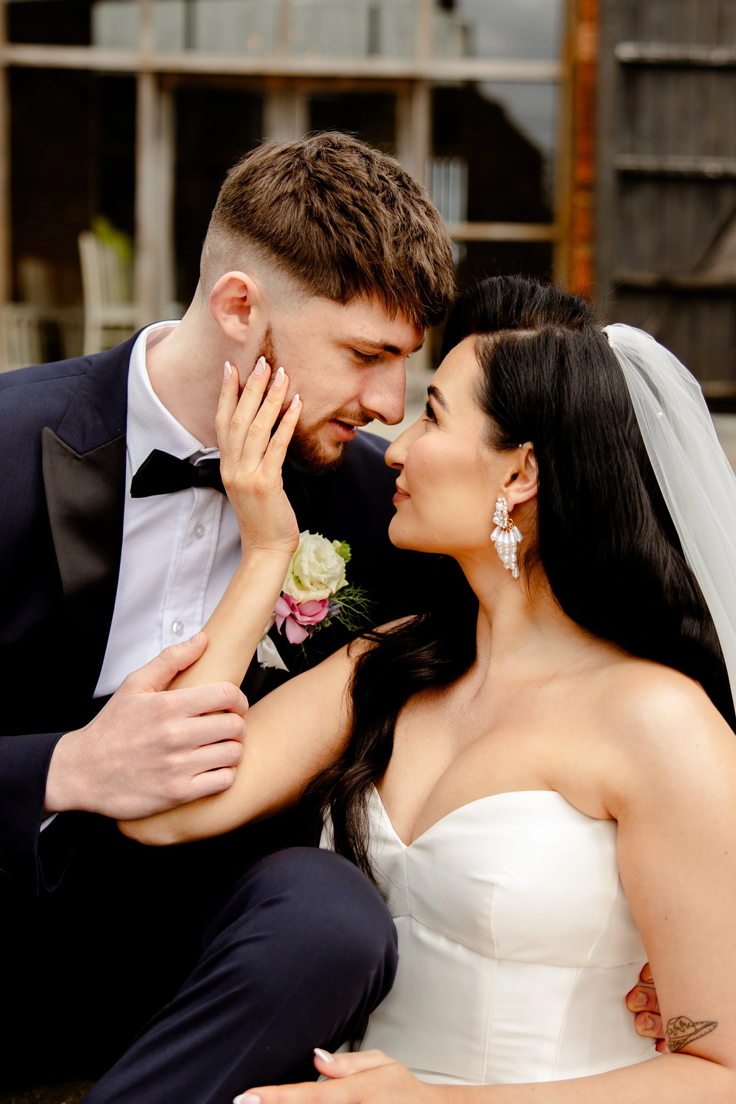 A bride and groom about to kiss, with the groom wearing a tuxedo and the bride in a strapless wedding dress, the bride touching the groom's face gently.