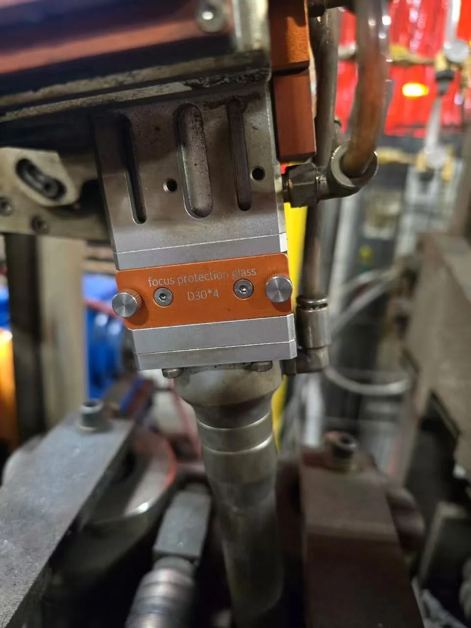 Close-up of an industrial machine part with focus protection glass label, in a manufacturing or workshop environment.