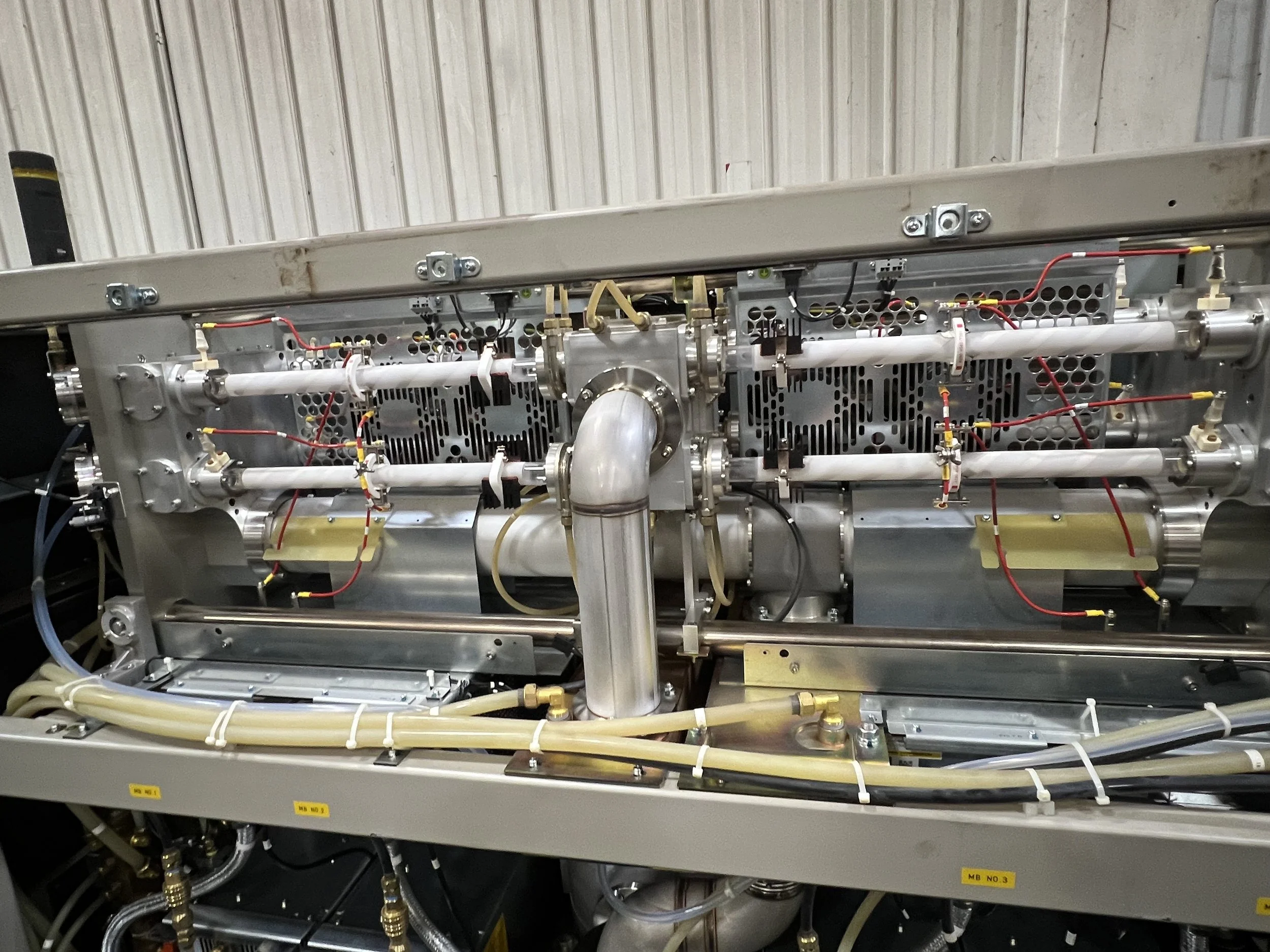 Close-up of a stainless steel scientific or aerospace equipment with multiple pipes, wires, and components mounted on a metallic frame.