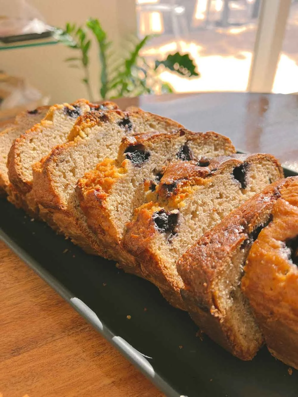 Slices of homemade banana bread with chocolate chips on a black rectangular plate on a wooden table.