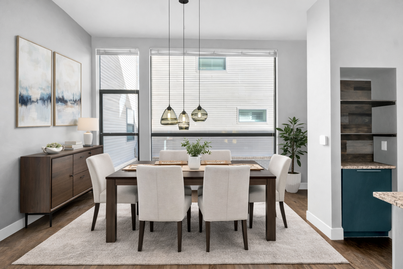 Modern dining room with a wooden table, six beige chairs, a sideboard with decorative items, and large windows with blinds