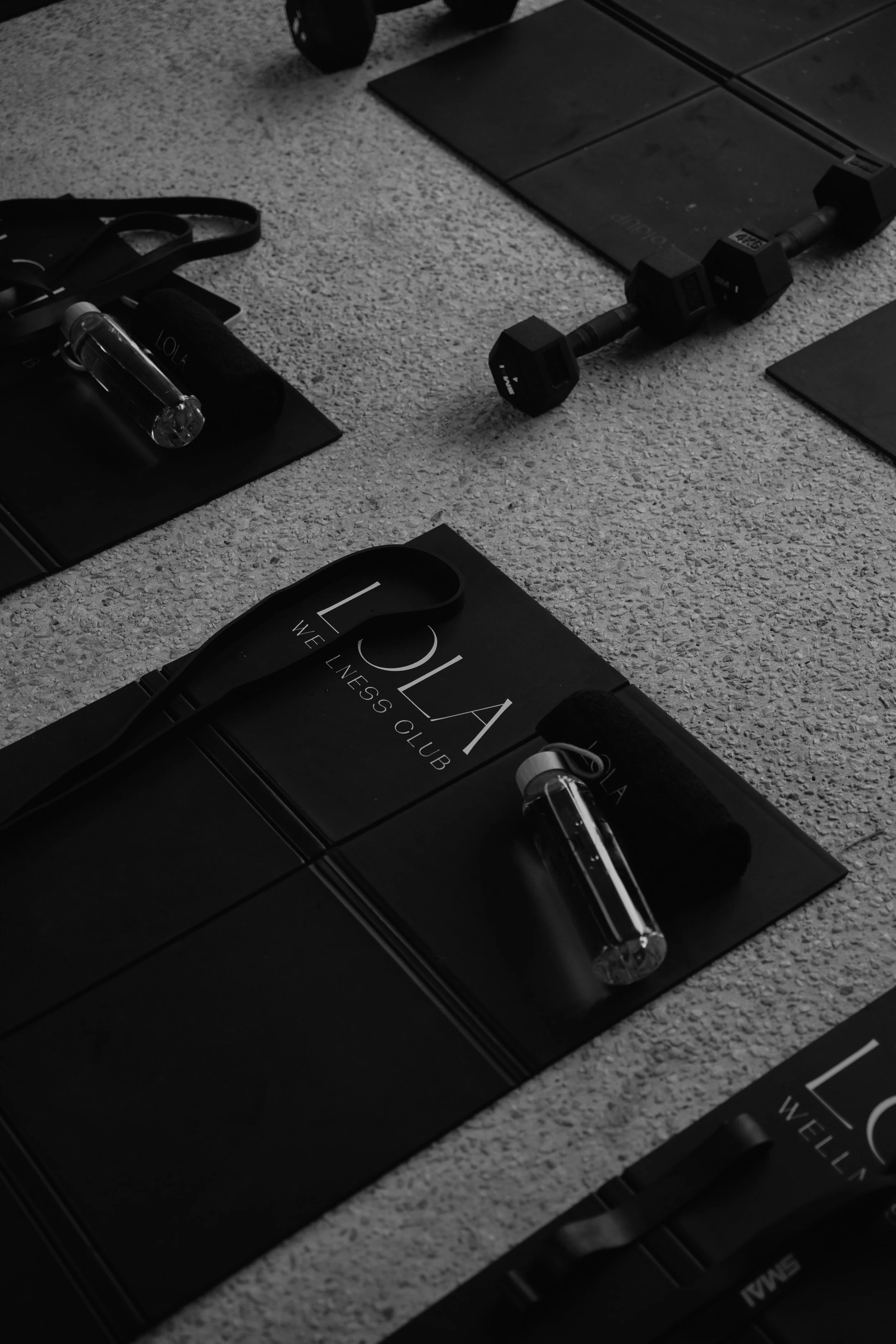 Workout items including a black gym bag labeled "LA FITA" with a water bottle, resistance band, and notebook, a set of dumbbells, and other fitness accessories arranged on a carpeted floor.