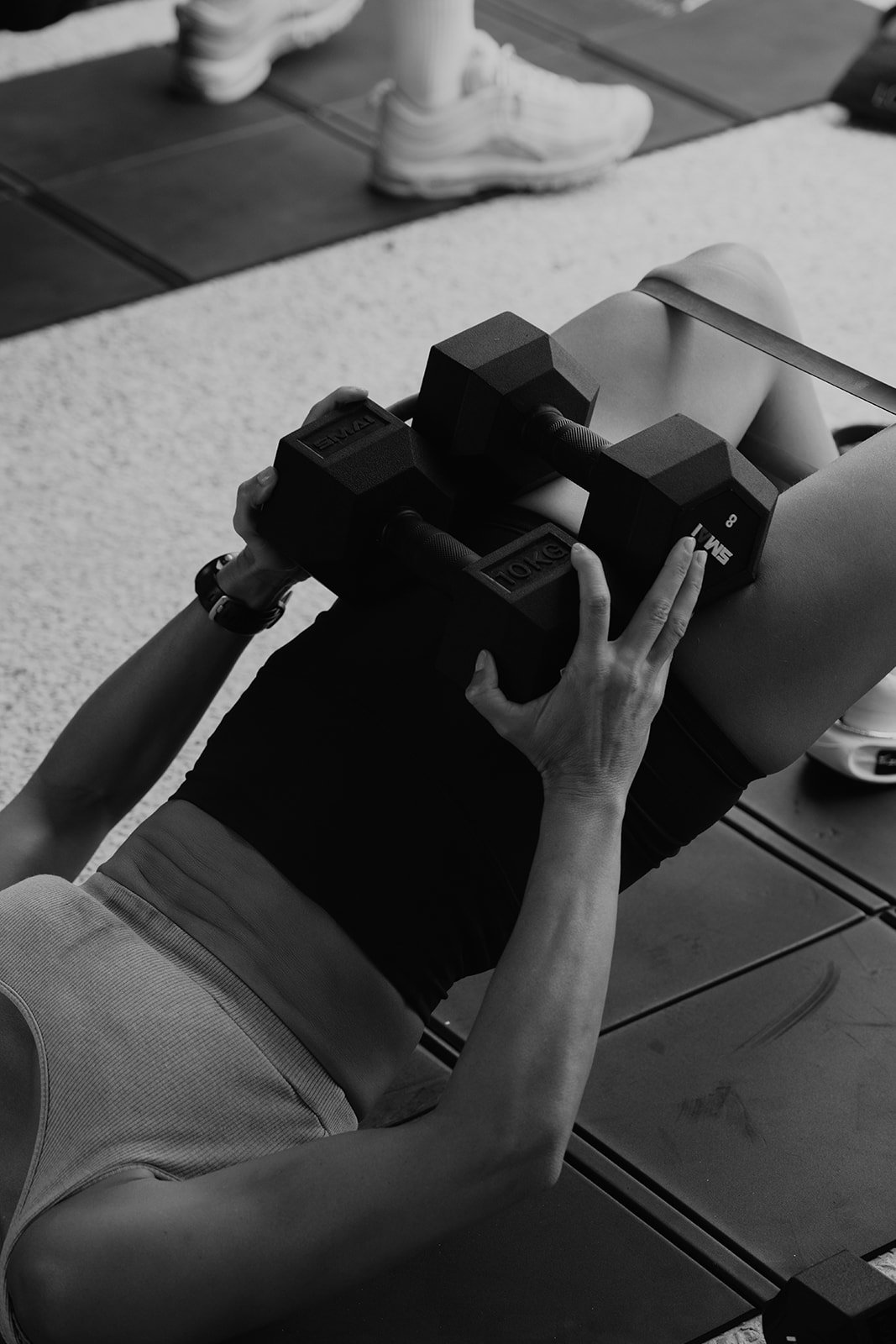 A person lying on a workout bench holding a dumbbell with both hands, performing a chest press exercise in a gym.