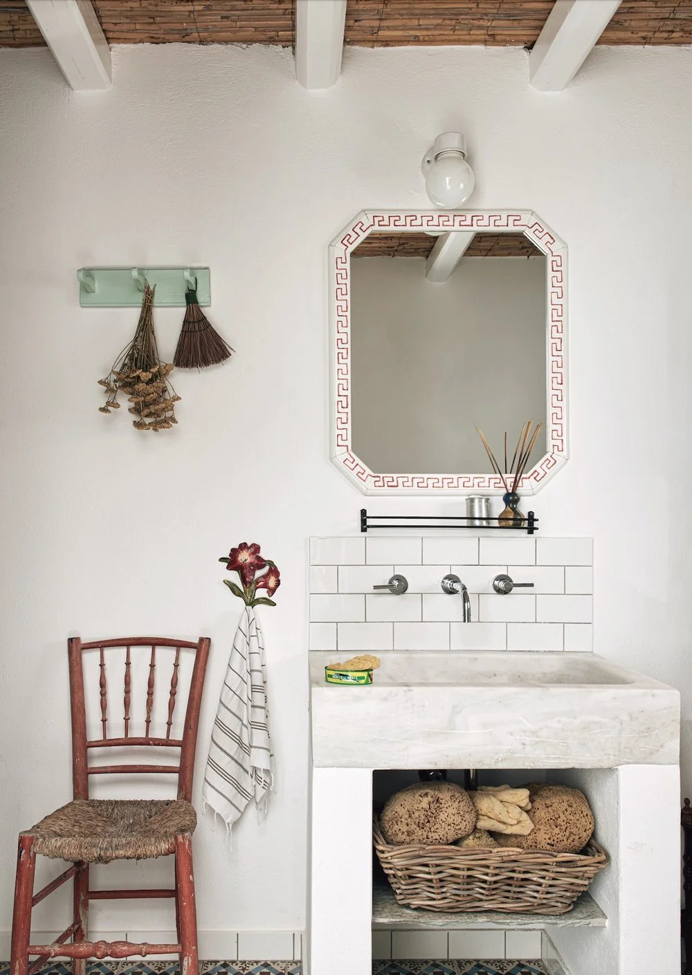 Eclectic Greek villa bathroom featuring patterned floor tiles, a vintage red wooden chair, and a bright blue door.
