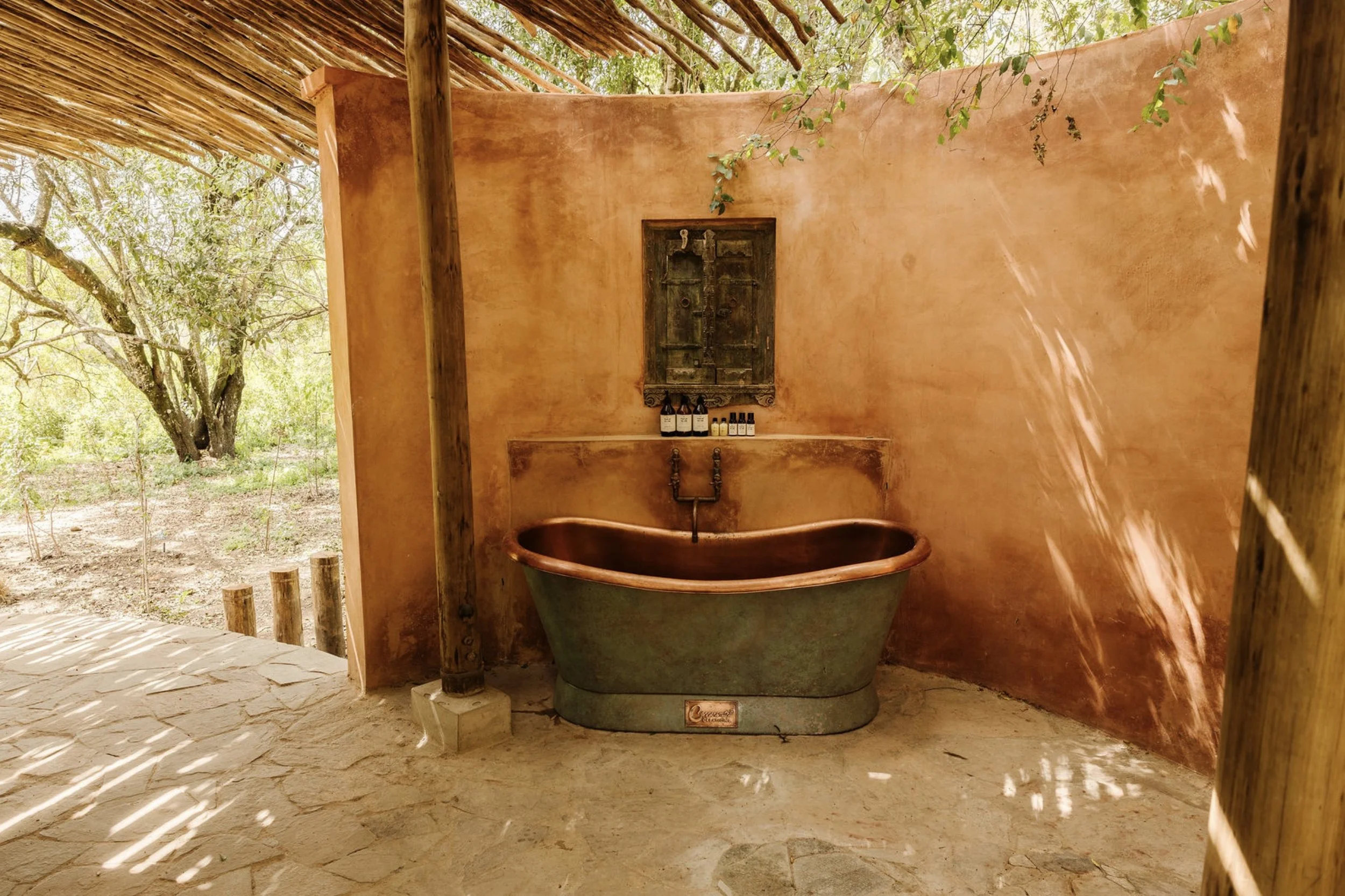 Rustic outdoor bathroom at a private safari lodge in Kenya featuring a freestanding copper bathtub and terracotta walls, designed by Howark Design.