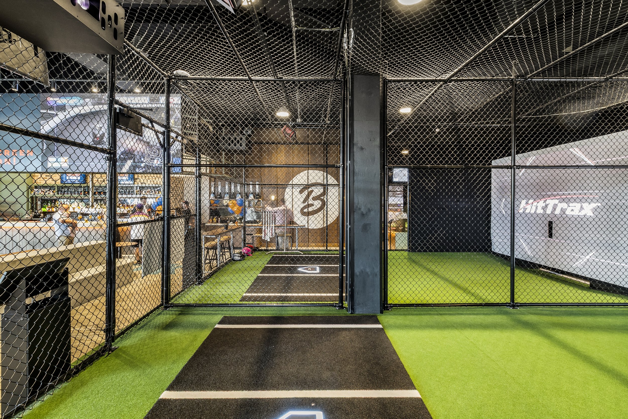 Indoor baseball batting cage with artificial turf floor, black safety netting, and a target home plate.