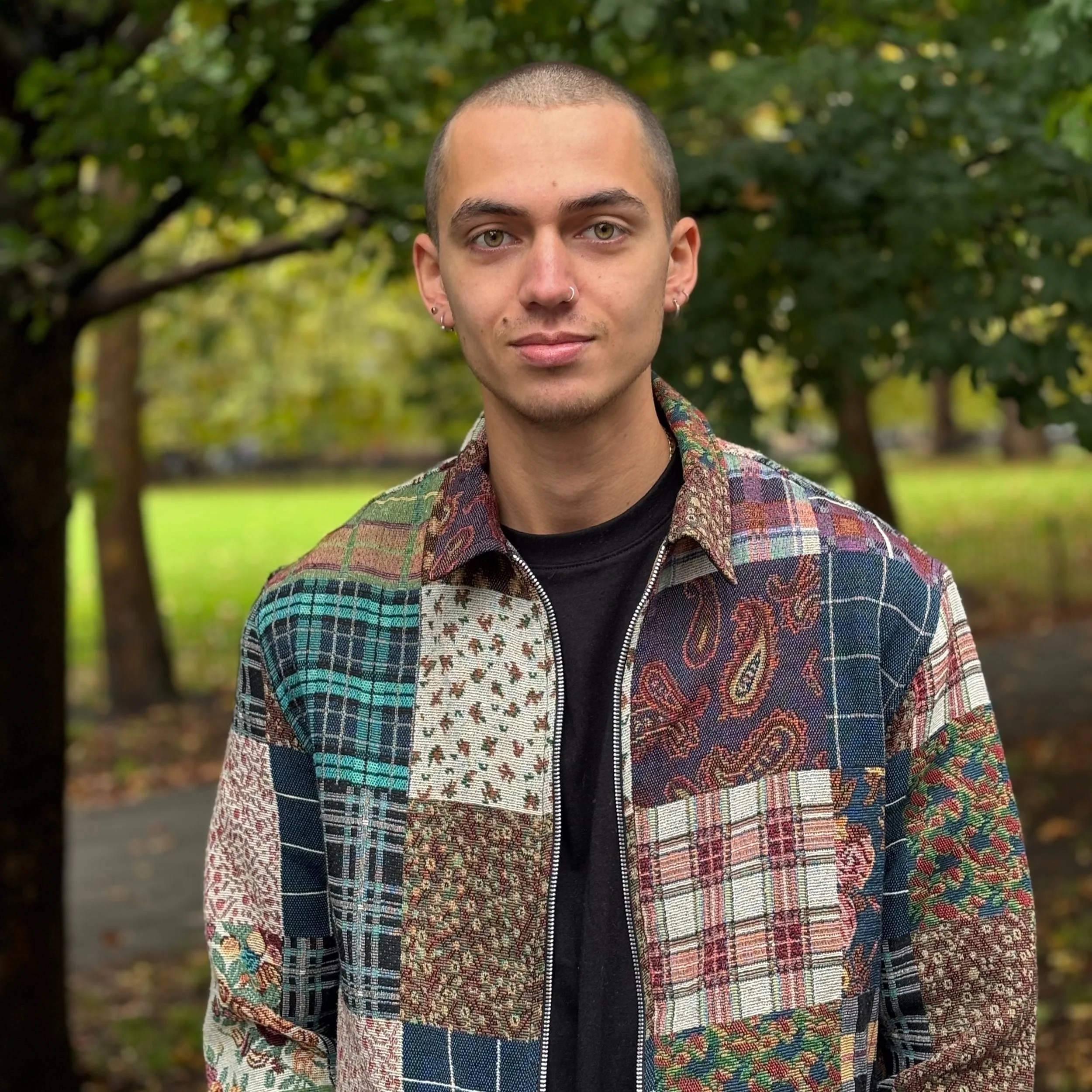 Charles is a white man in his twenties with a shaved head. He has a nose ring, green eyes and wears a black tee under a patterned jacket