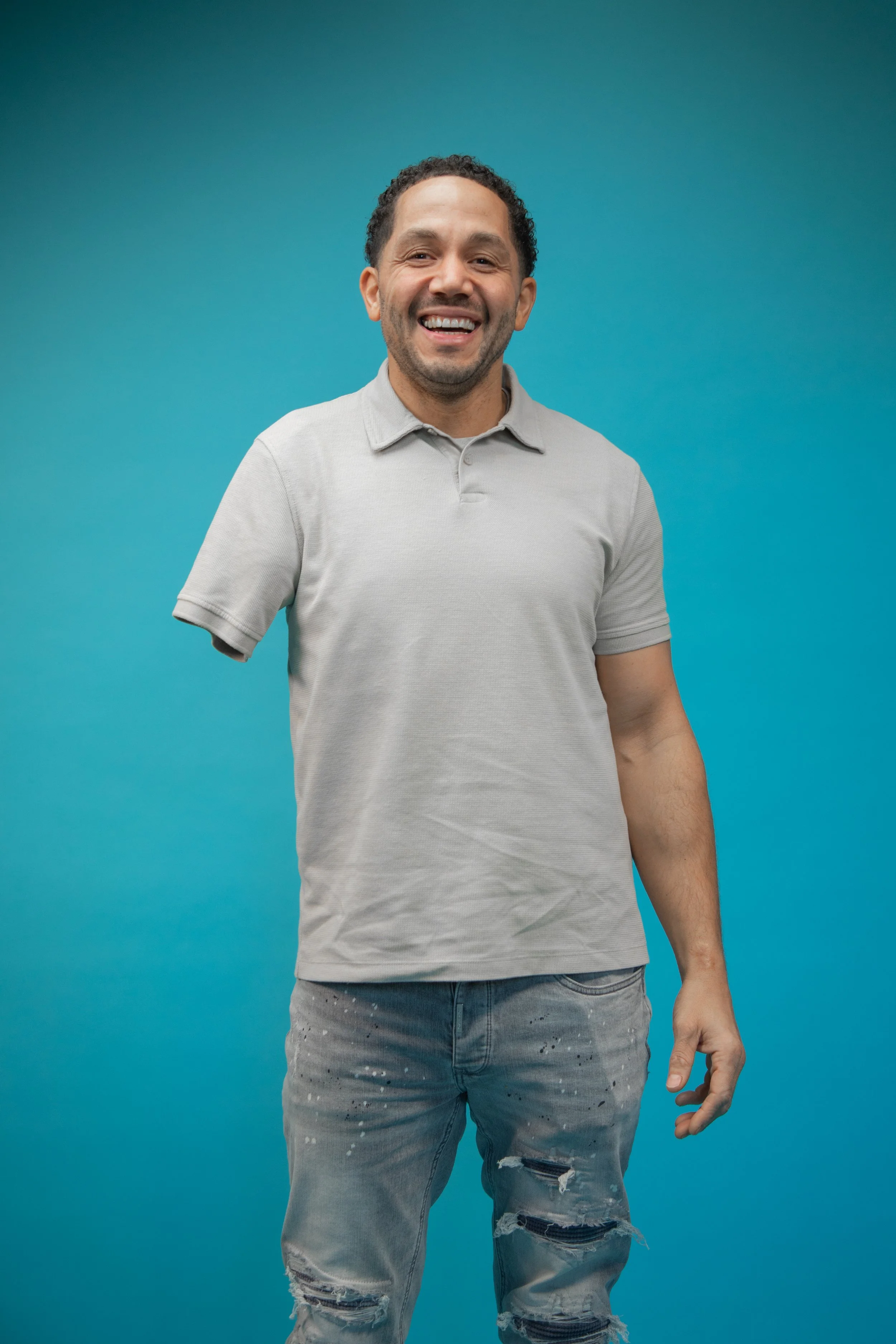 Chris is stood facing the camera smiling widely with his arm by his side.