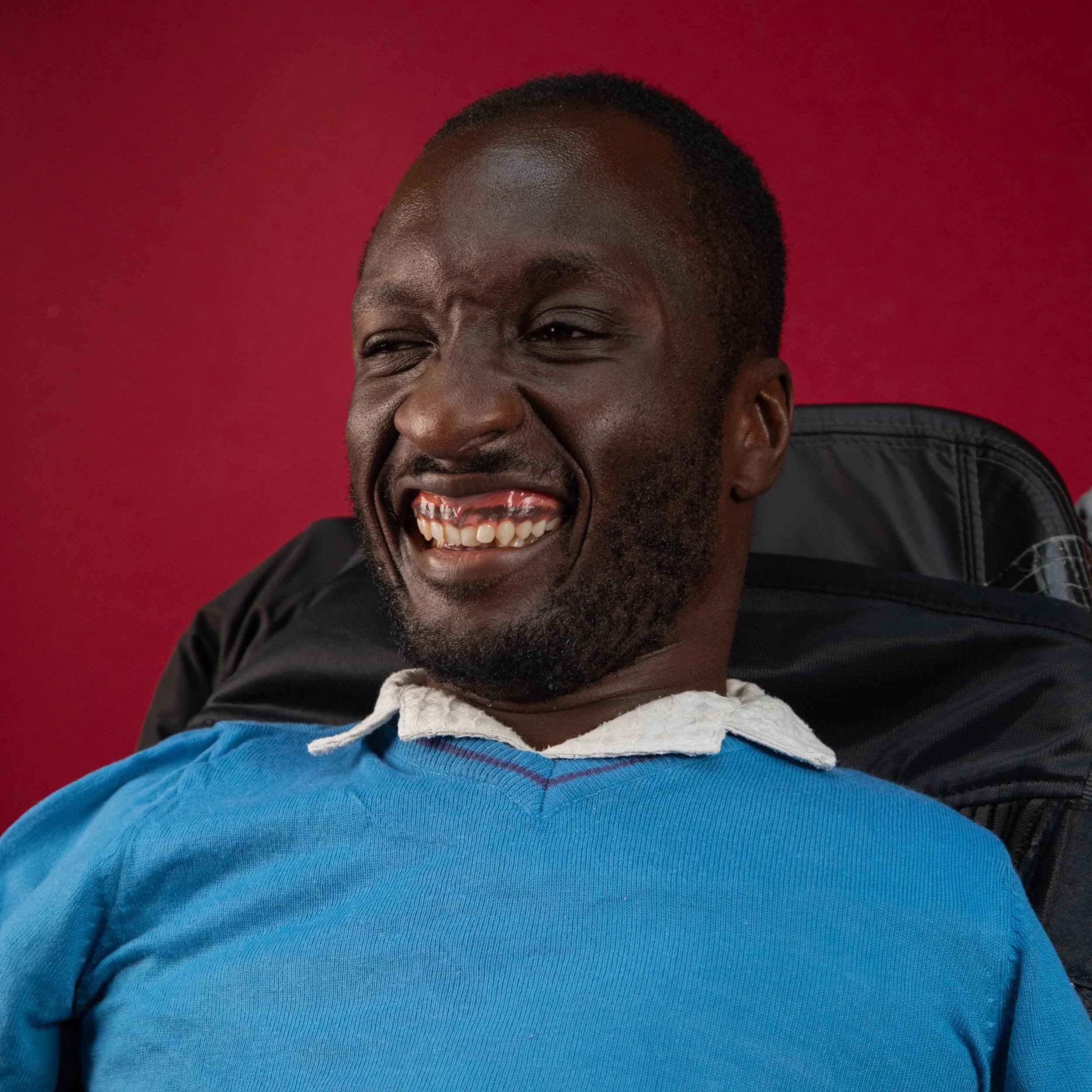 Isaac is a Black man with short shaved dark hair. He is smiling widely, showing his teeth. He's sat in his power wheelchair.