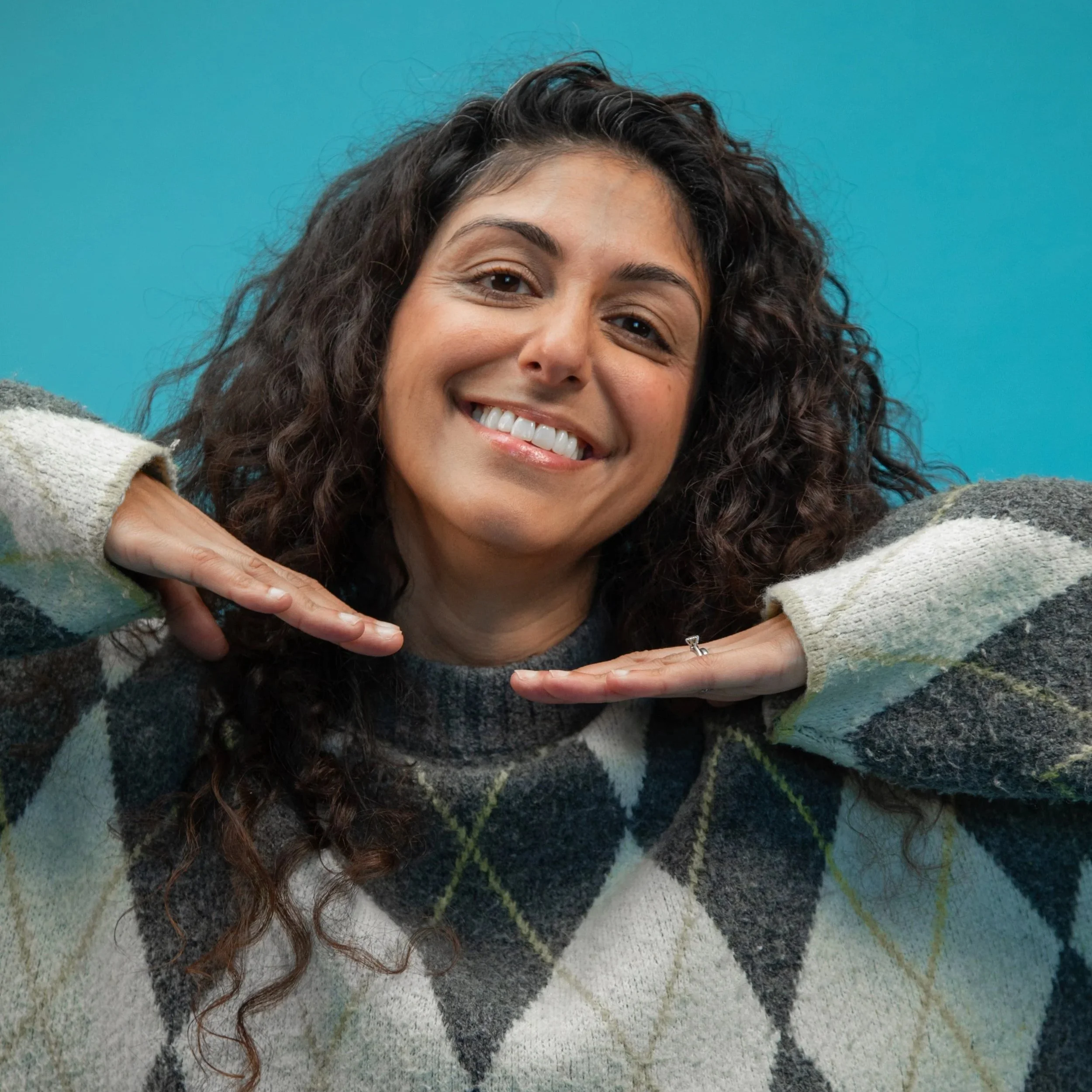 Amanprit is smiling widely with her hands placed under her chin and her elbows out.