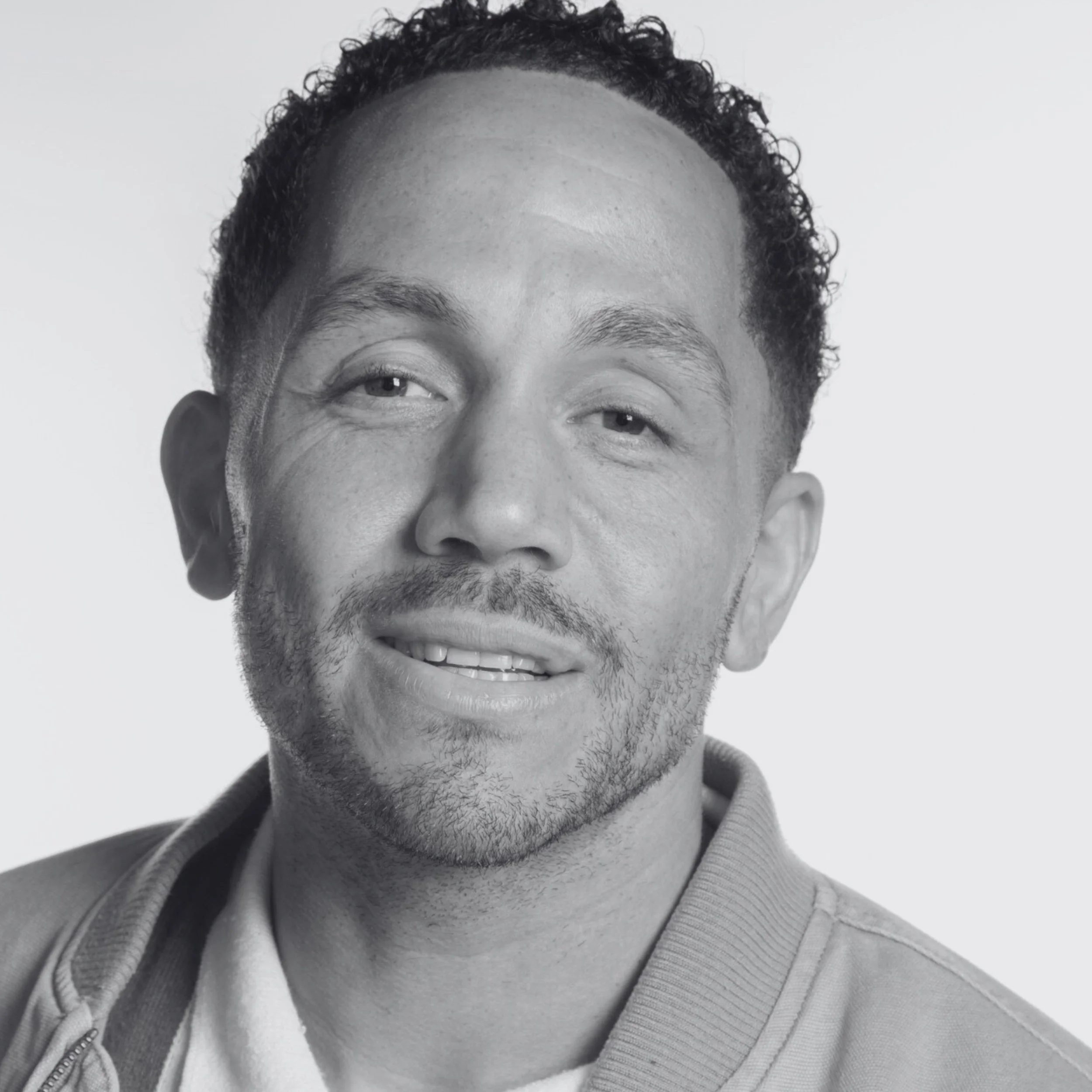 Chris is a mixed race man with dark shot curly hair and brown eyes. He has stubble and is looking directly into the camera