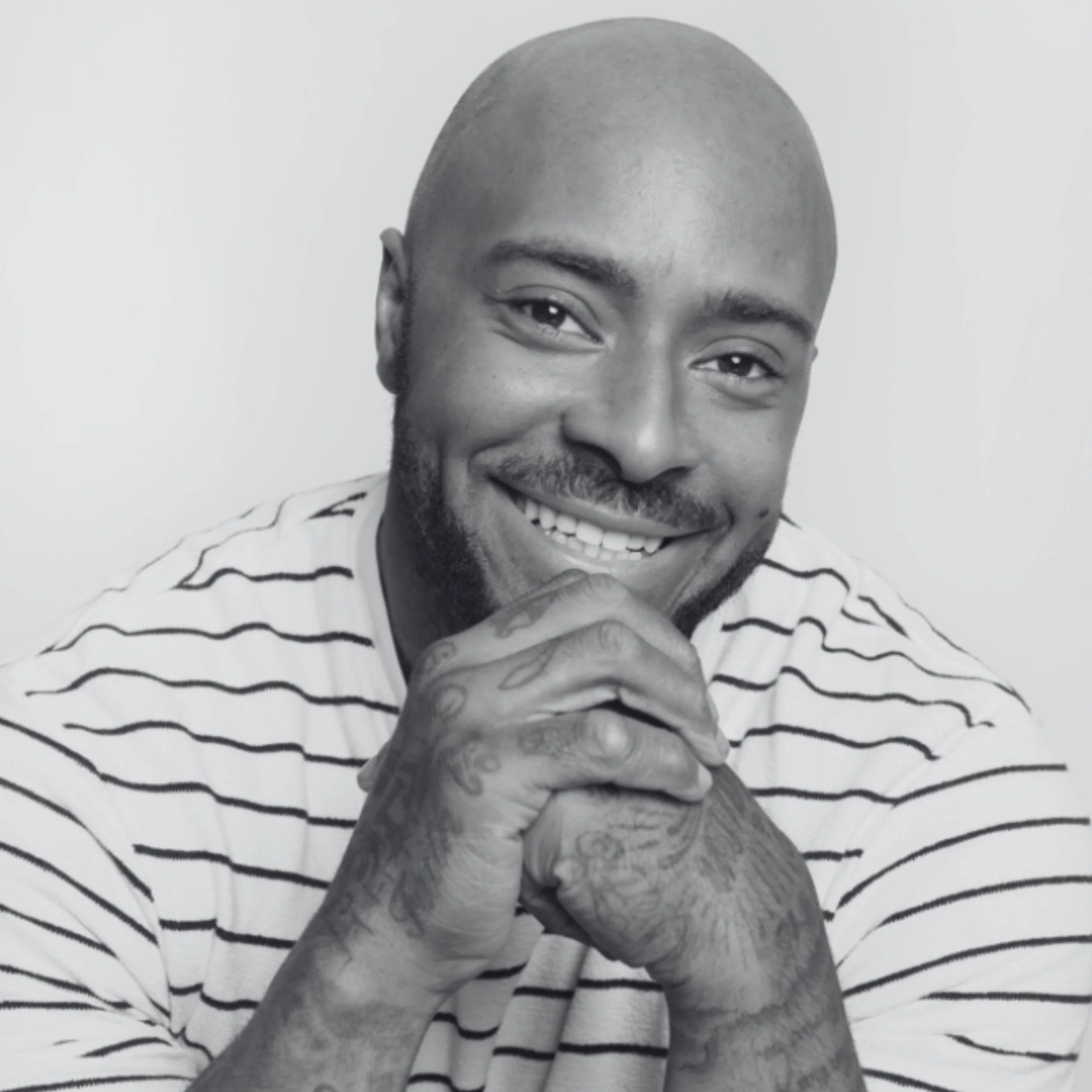 Ash is a Black man with brown eyes. His head is bald, he has a short beard and a warm smile