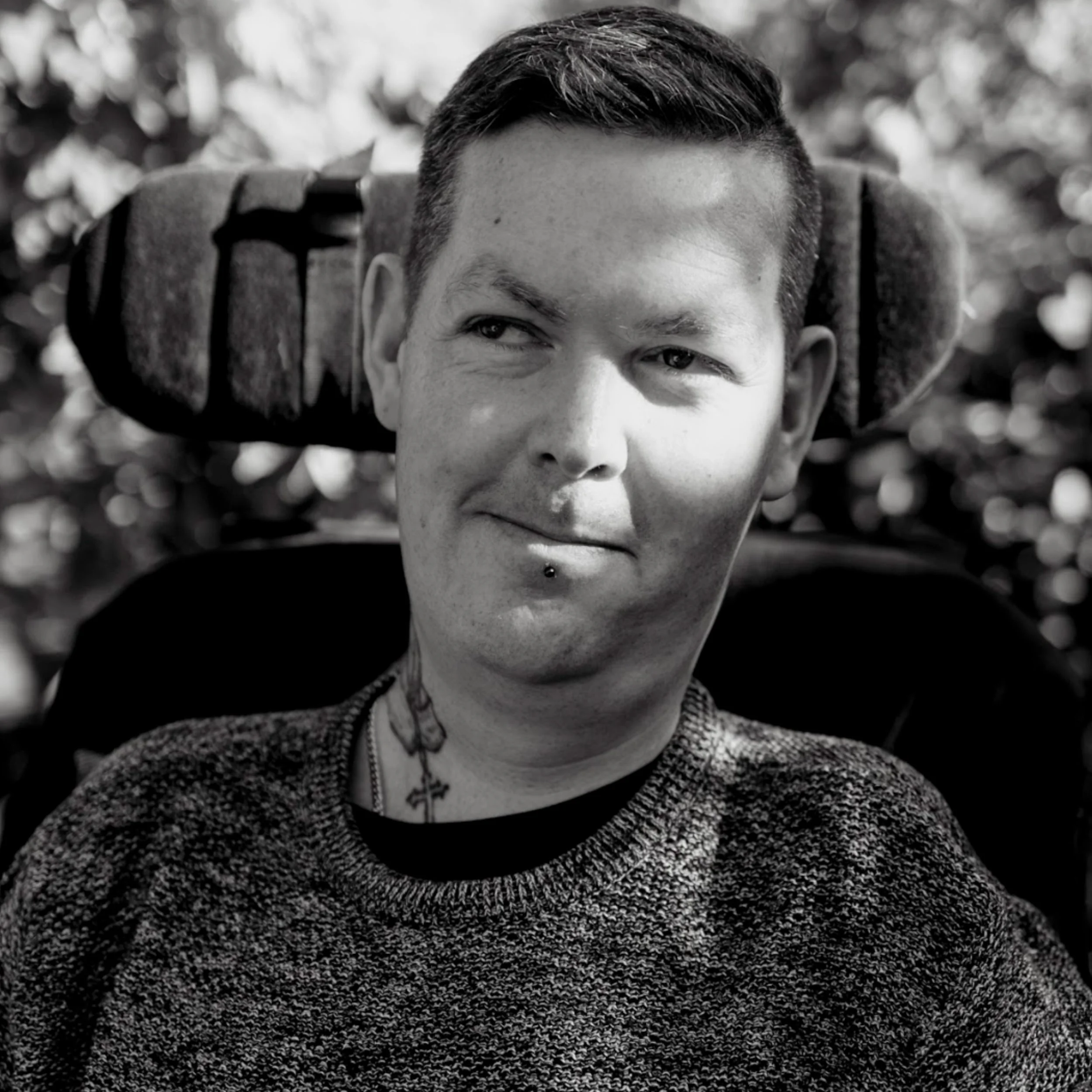 Luis is a white man sitting in his power wheelchair. He has short brown hair, a neck tattoo and a lip piercing