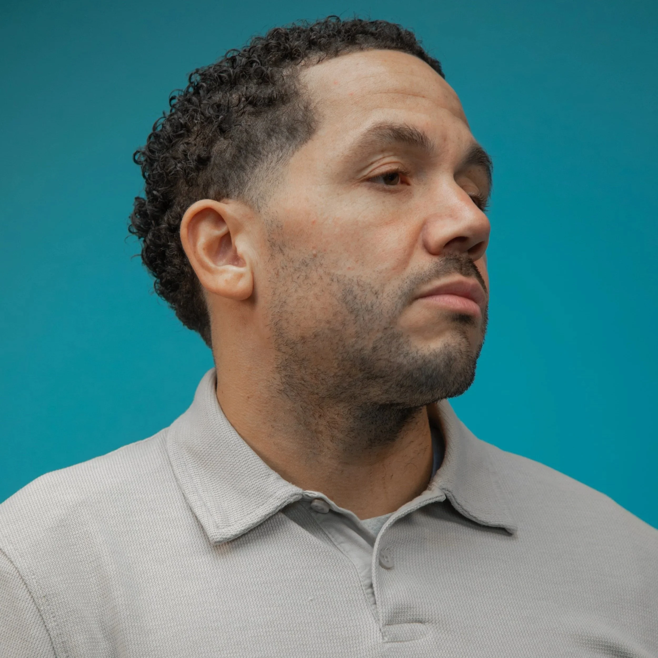 A close-up side profile of Chris looking to the side. He has dark stubble and his expression is neutral.