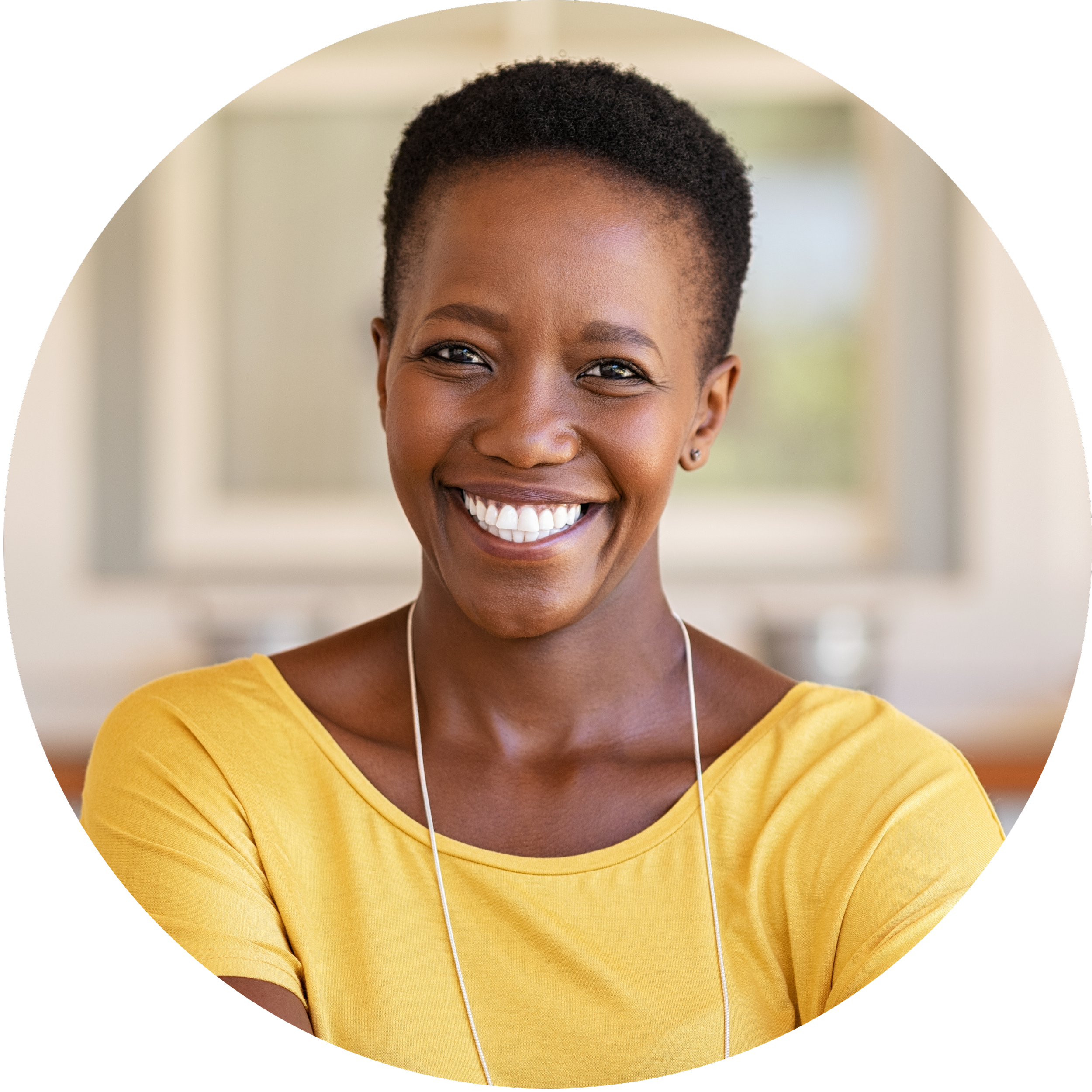 A smiling Black woman with short hair wearing a yellow top, standing indoors.
