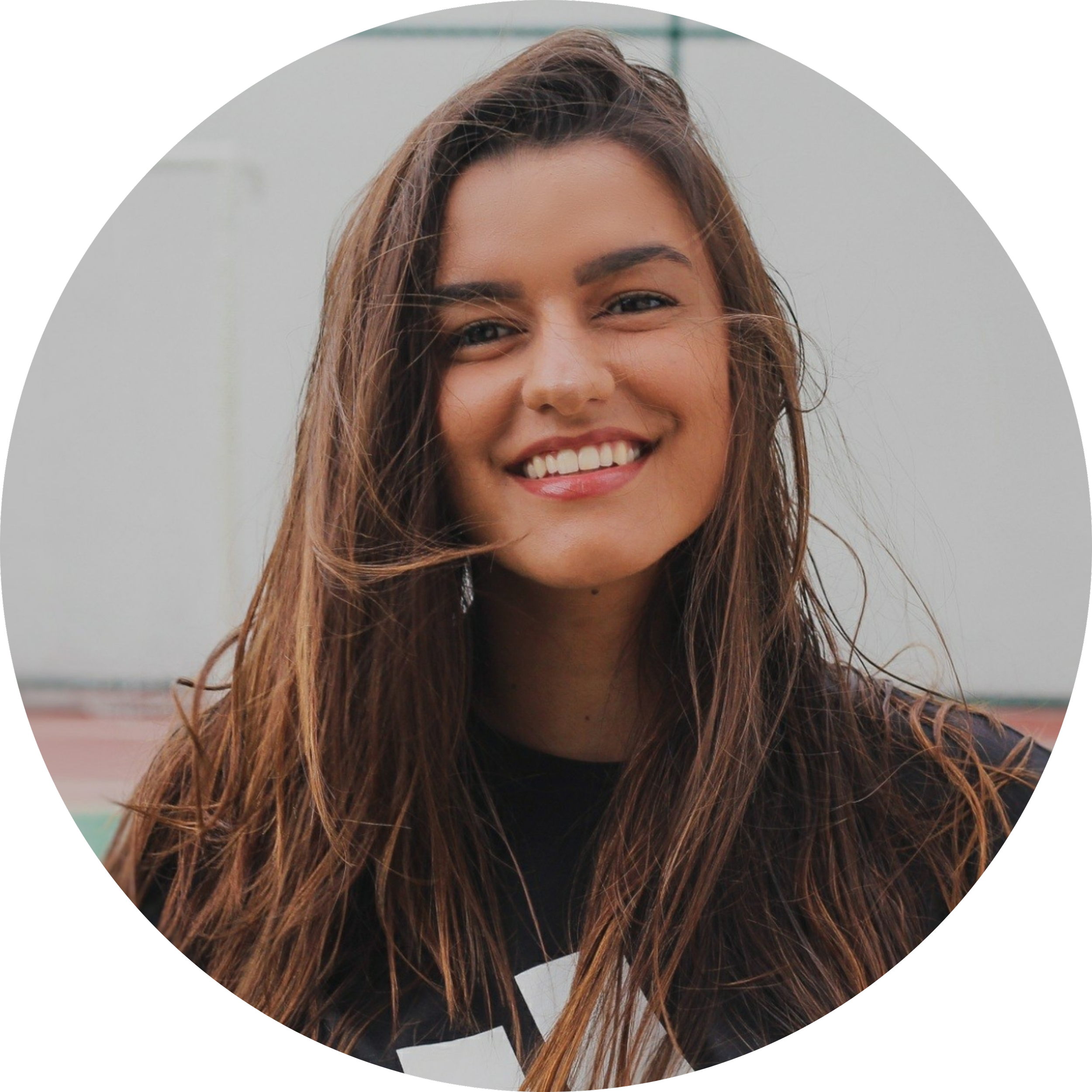 Close-up of a young woman with long, wavy brown hair smiling outdoors during daytime.