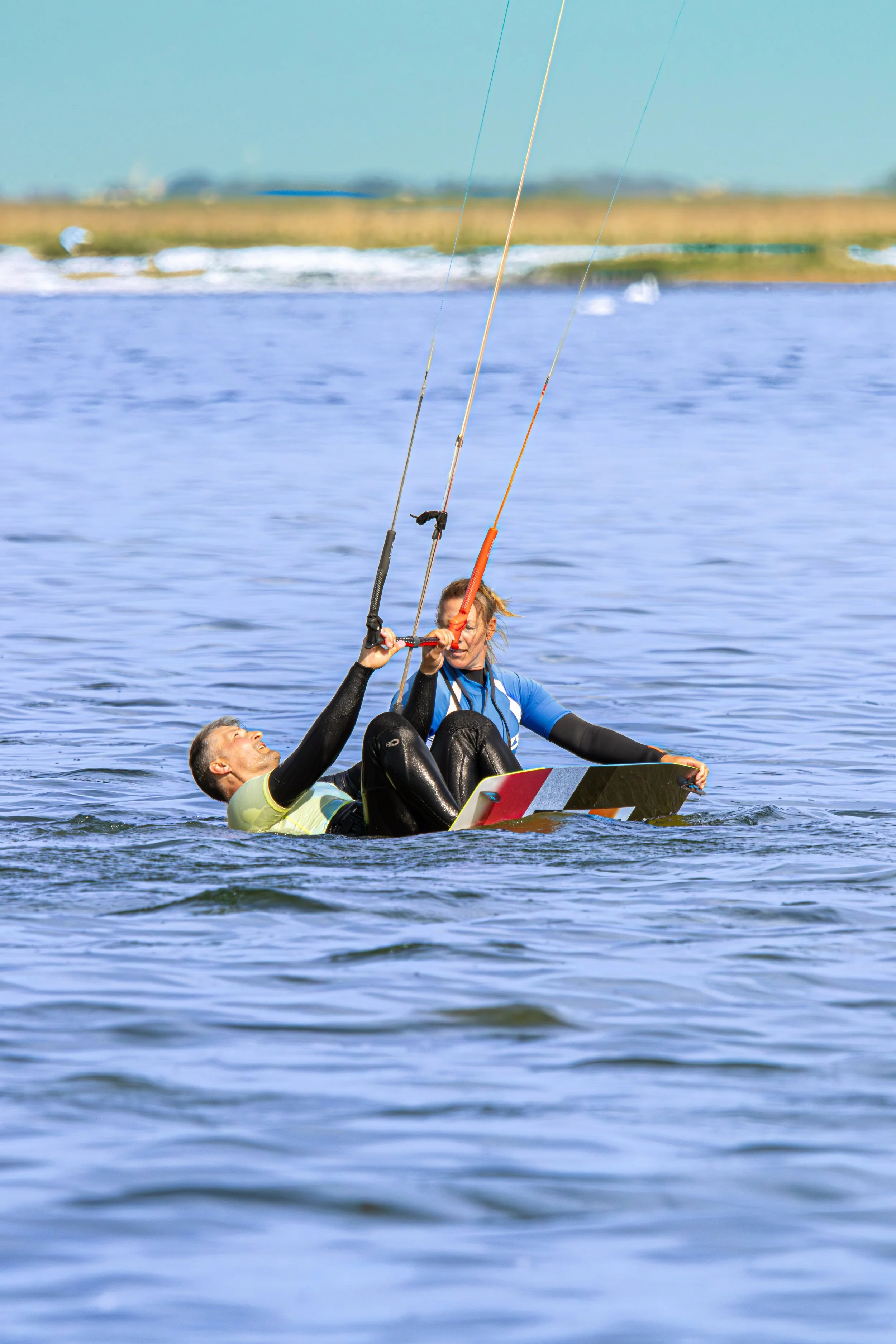 Twee mensen kiten op het water, één ligt onder en de ander zit op een board, samen balancerend en in evenwicht houden tijdens kite surfen.