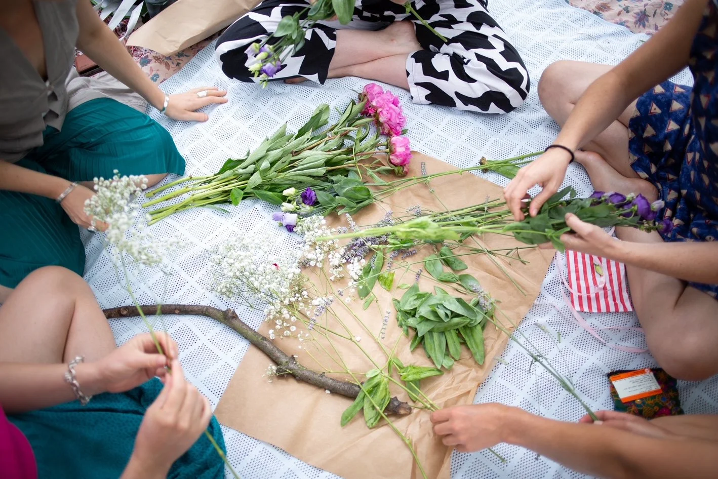 Group of people arranging flowers on a white patterned blanket during a flower arranging activity.
