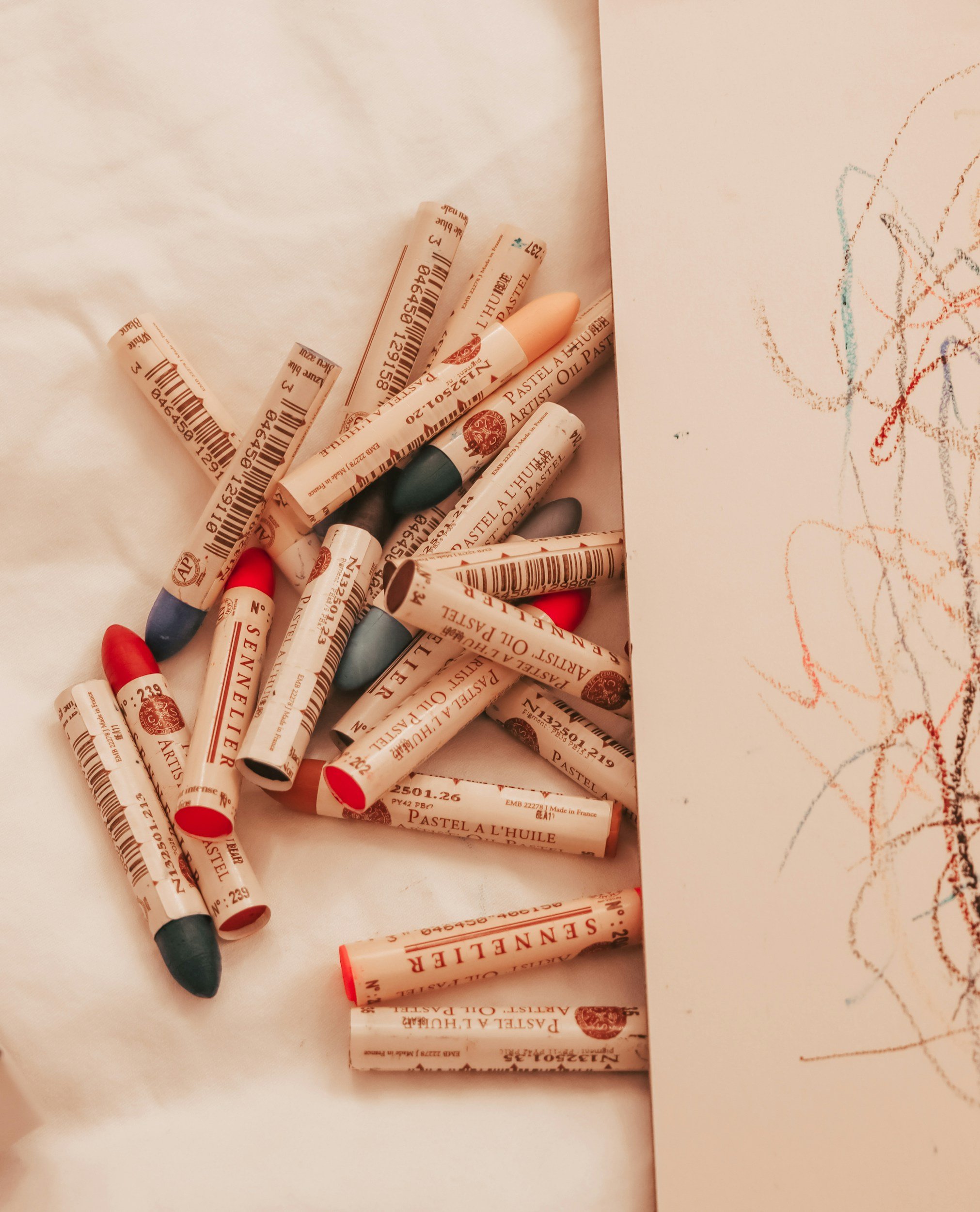 Cream colored paper with children's drawings on the right side and scattered lip crayons in various colors on the left side.