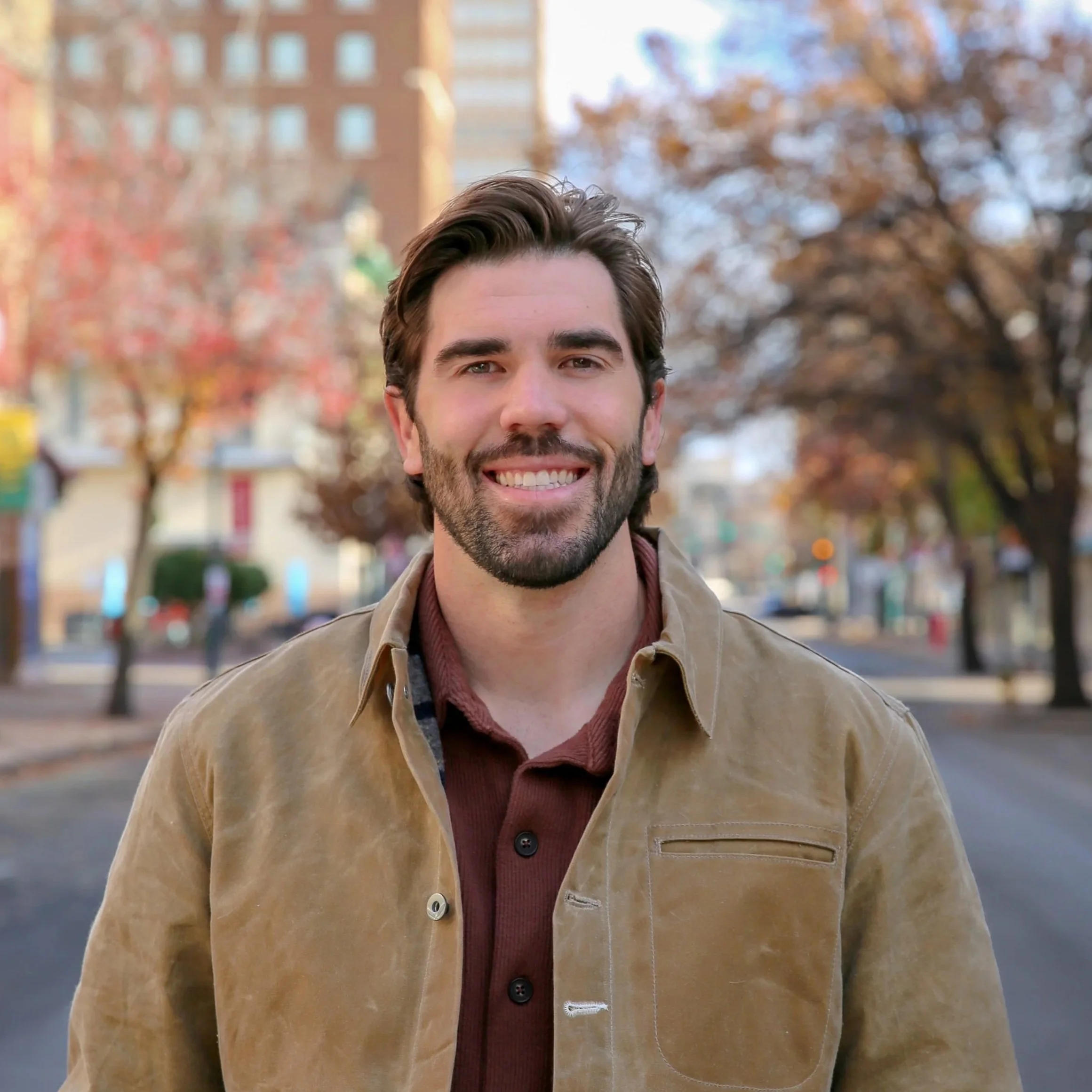 Trevor Caswell Waco TX Realtor posing in downtown Waco, TX wearing a tan leather jacket and burnt orange button down.
