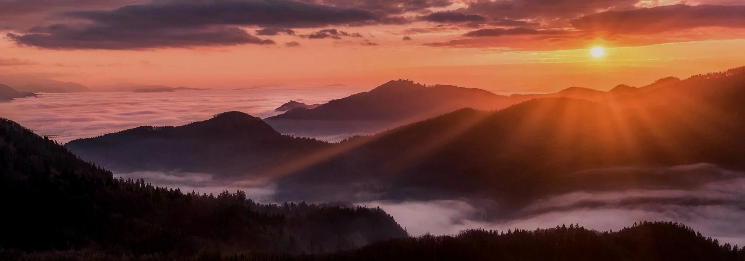Sunrise over layered mountain ridges with soft clouds settled in the valleys, symbolizing a calm and reflective beginning to the year.