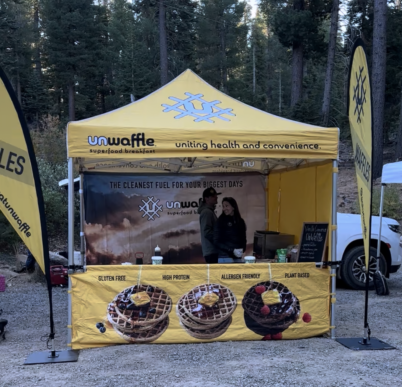 Yellow Unwaffle vendor tent at an outdoor mountain event with waffle displays and branding, reflecting the company’s connection to endurance events and on-the-go wellness.