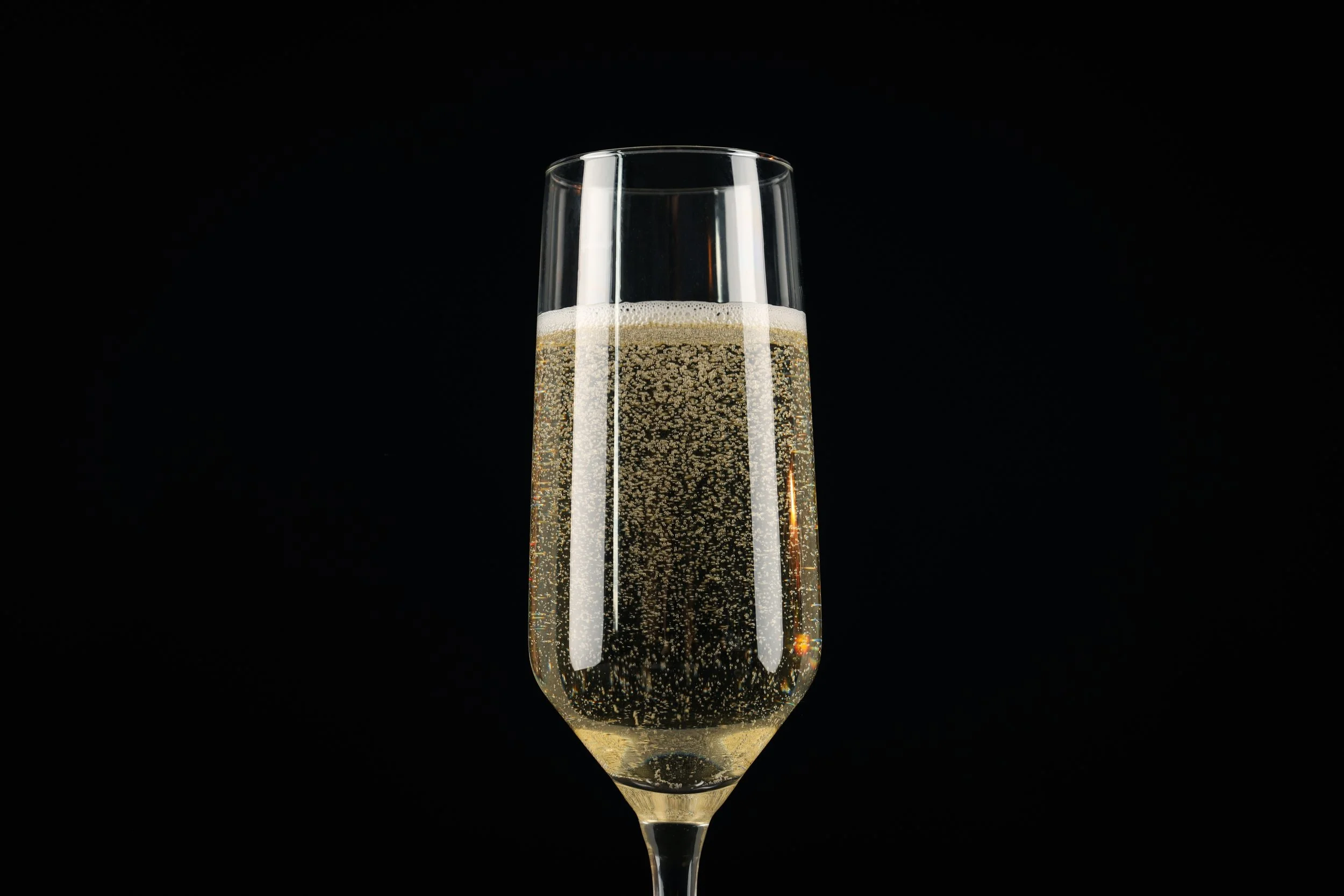 Close-up of a Champagne flute filled with sparkling Champagne against a black background, with bubbles rising through the glass and a light foam at the top