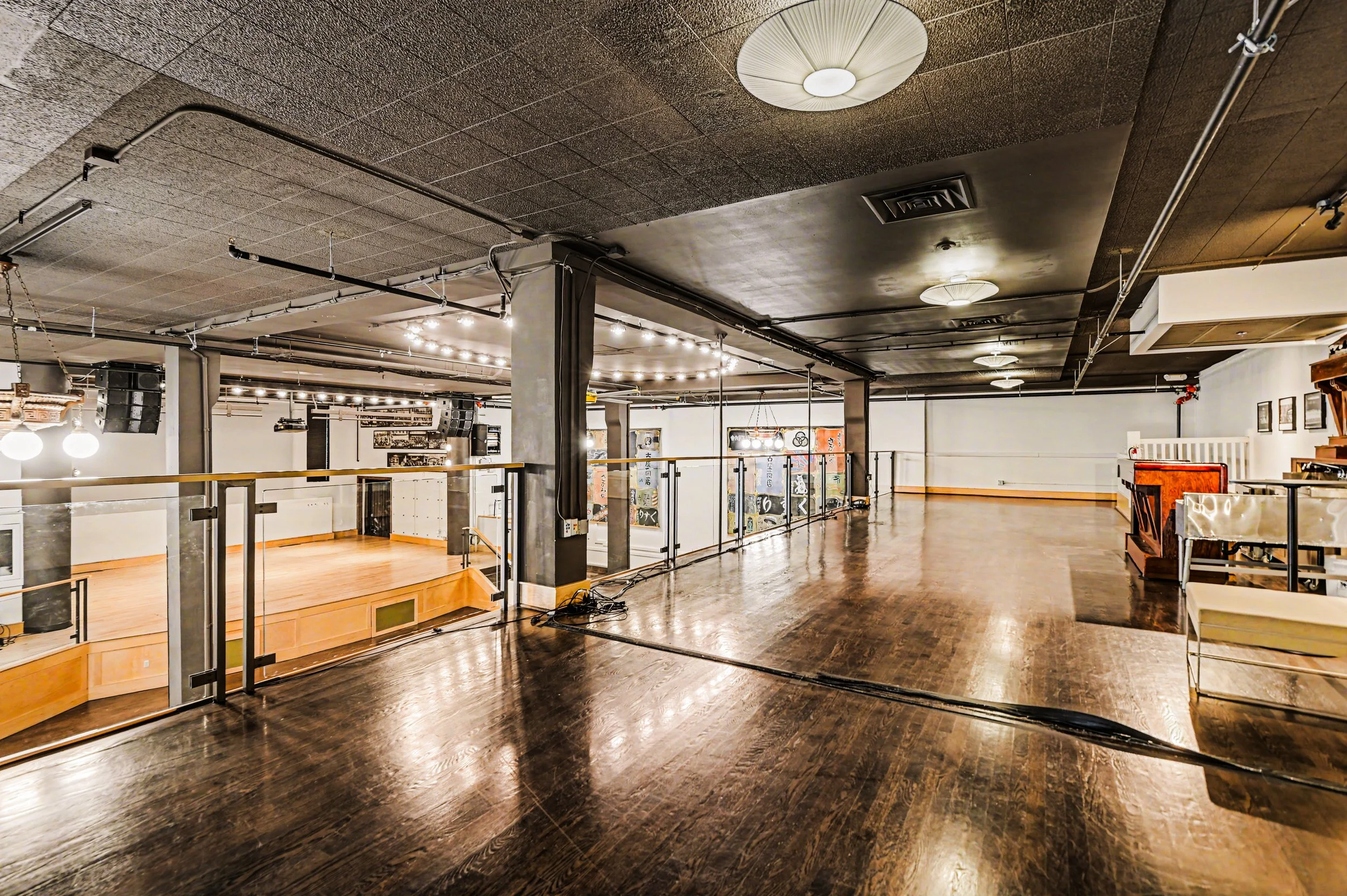 Nippon kan theatre, seattle, washington, event space, wedding,Empty upstairs interior space with hardwood flooring, black ceiling, various lighting fixtures, and a partial view of a lower level with a stage and decorations.