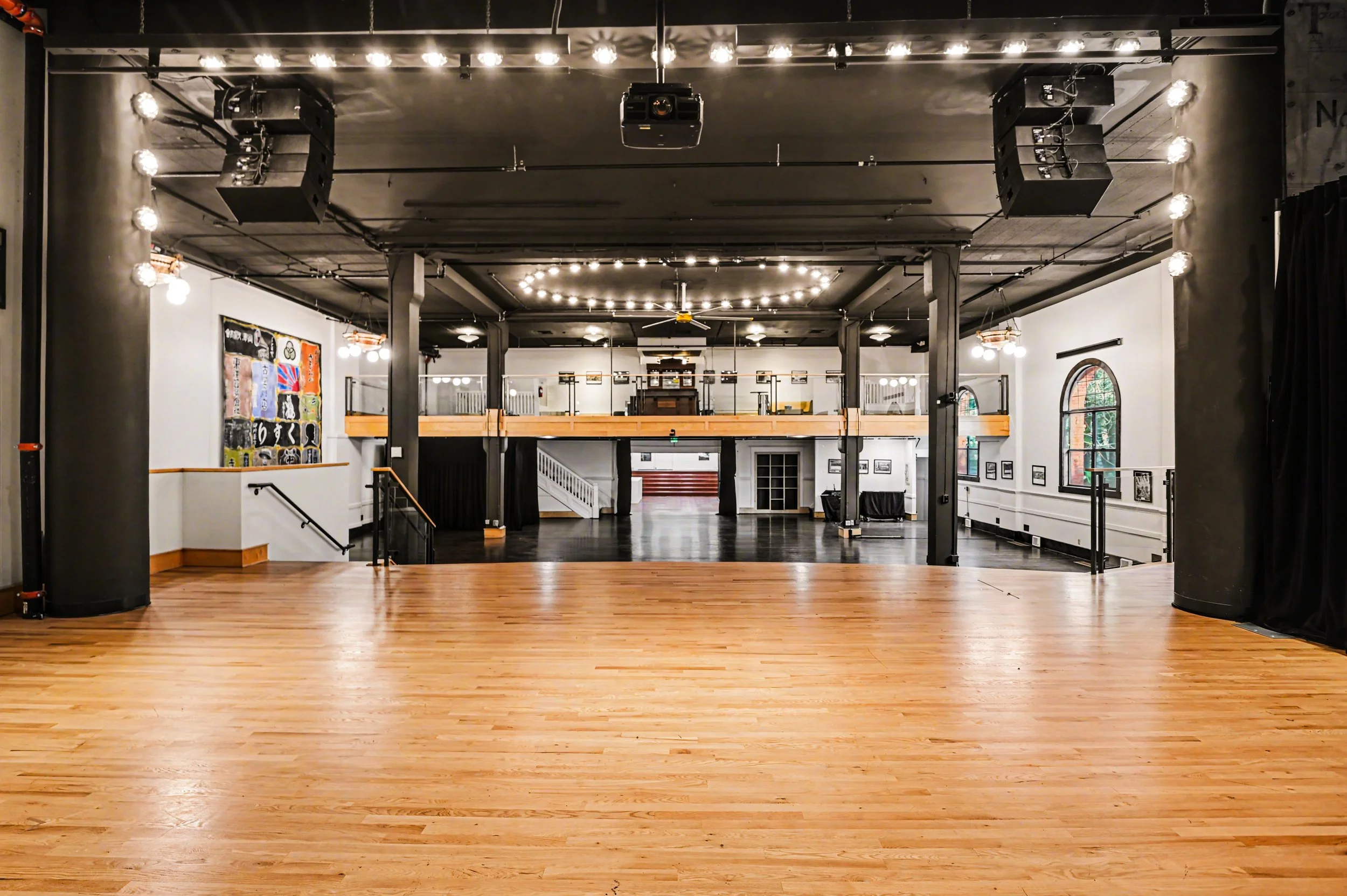 Nippon kan theatre, seattle, washington, event space, wedding,Empty dance hall with wooden floors, black ceiling beams, art on the walls, and string lights hanging from the ceiling.