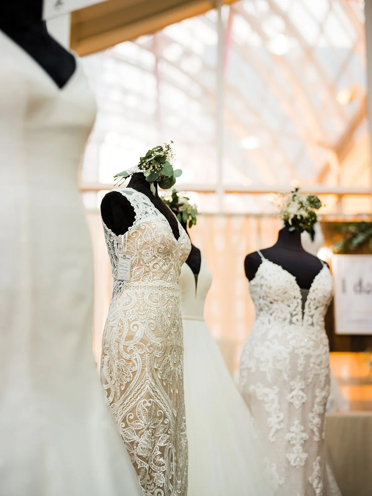 Display of three wedding dresses on black mannequins inside a boutique, with large windows in the background allowing natural light.