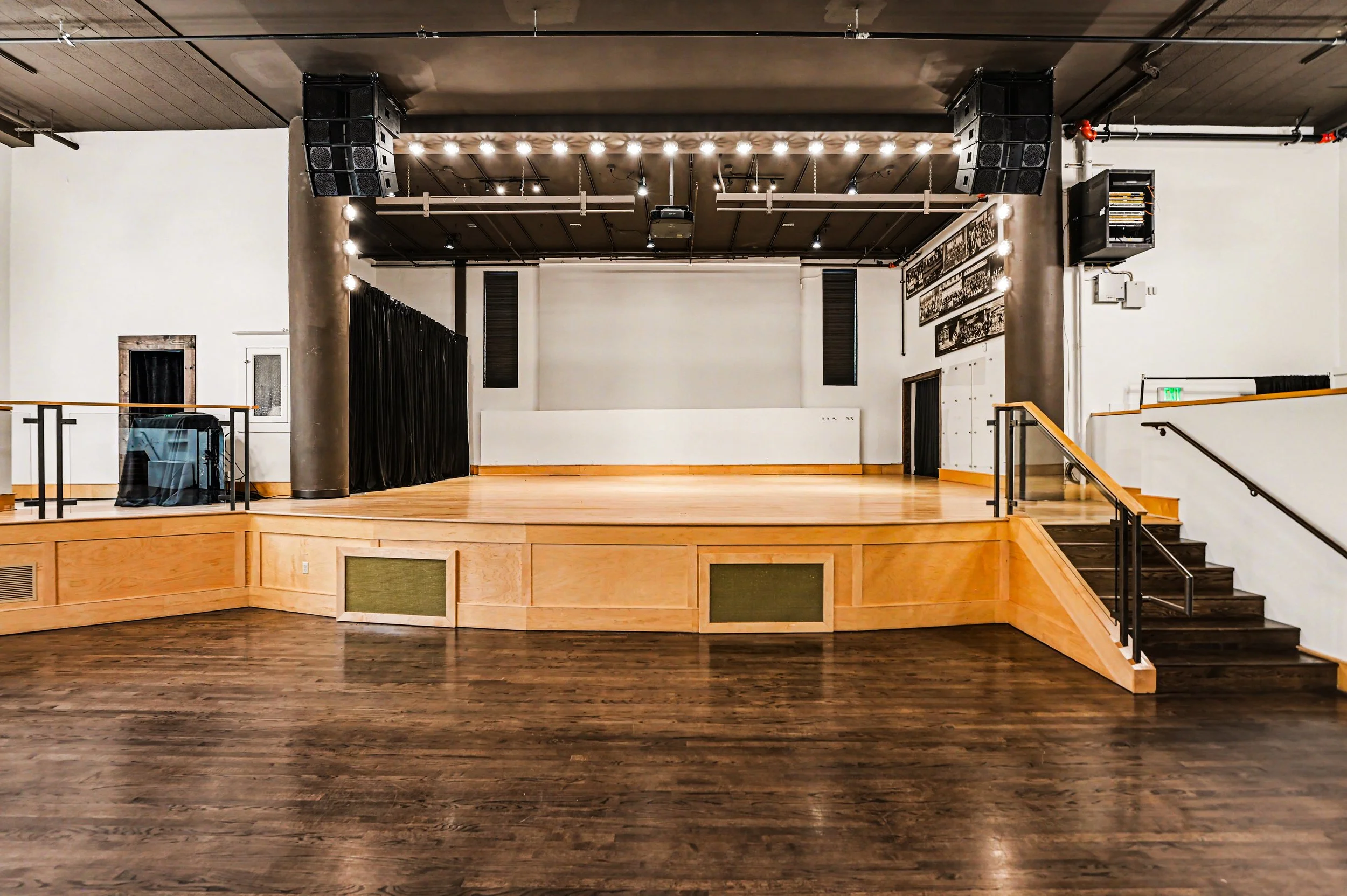 Nippon kan theatre, seattle, washington, event space, wedding,An empty indoor stage with a wooden floor, black curtains on one side, wall-mounted speakers, and framed photographs on the wall, prepared for a performance or event.