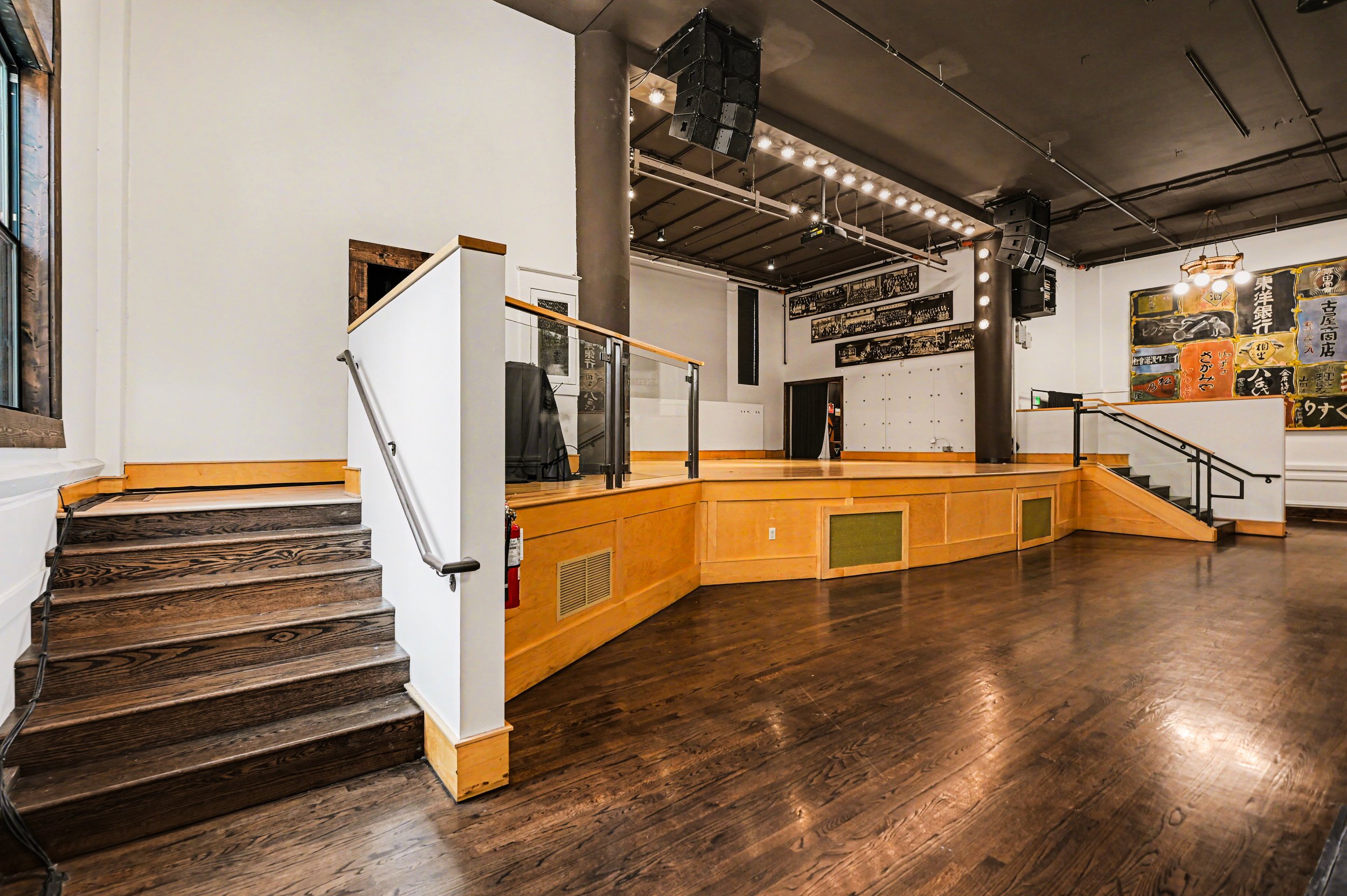 Nippon kan theatre, seattle, washington, event space, wedding,Empty stage area with wooden flooring, stairs, black ceiling, and artwork on the walls.