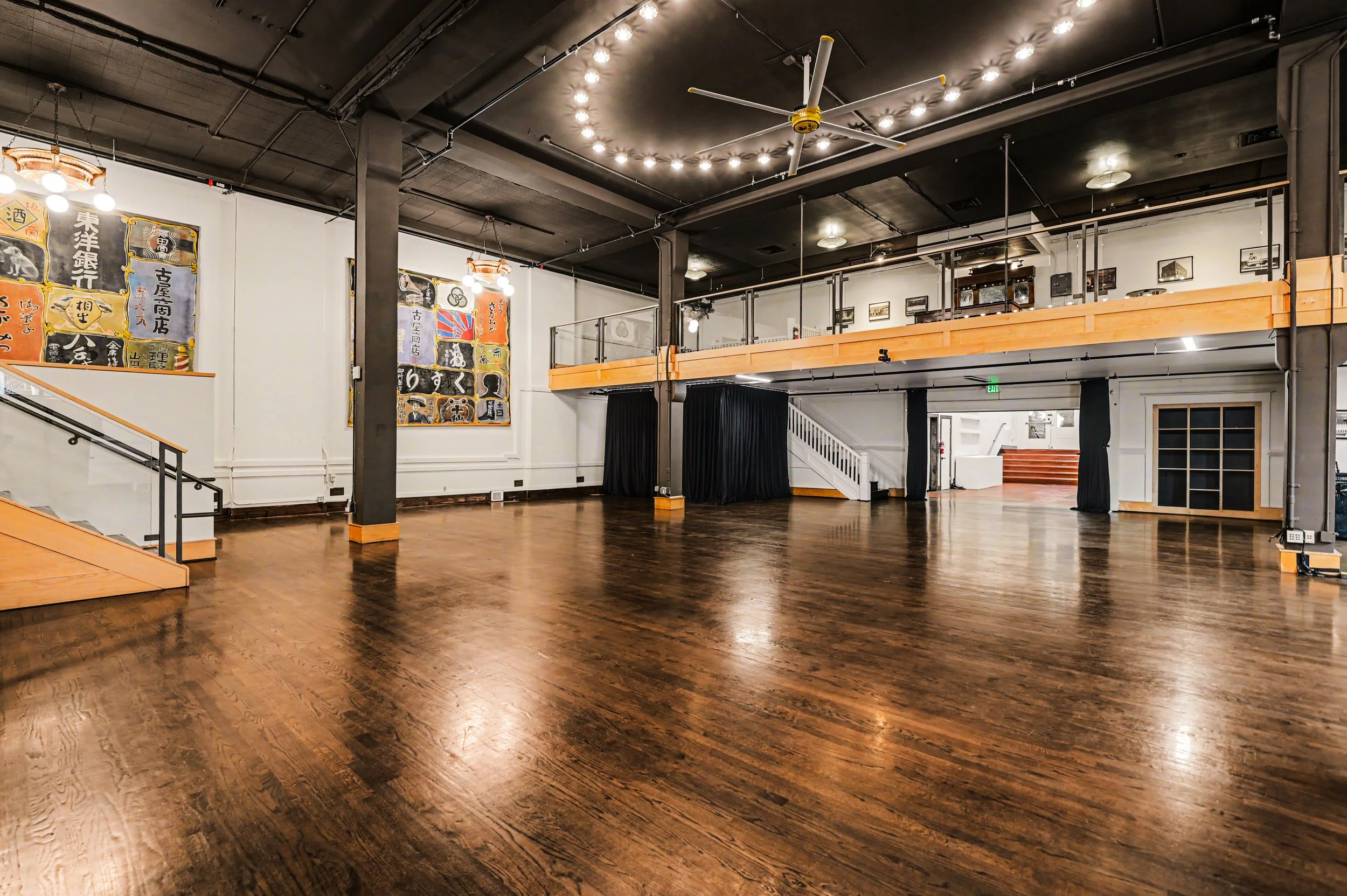 Nippon kan theatre, seattle, washington, event space, Empty interior of a modern event space or studio with wooden floors, black ceiling, and a second-floor balcony. Decor includes artwork with Japanese characters, ceiling fan, and lighting fixtures.