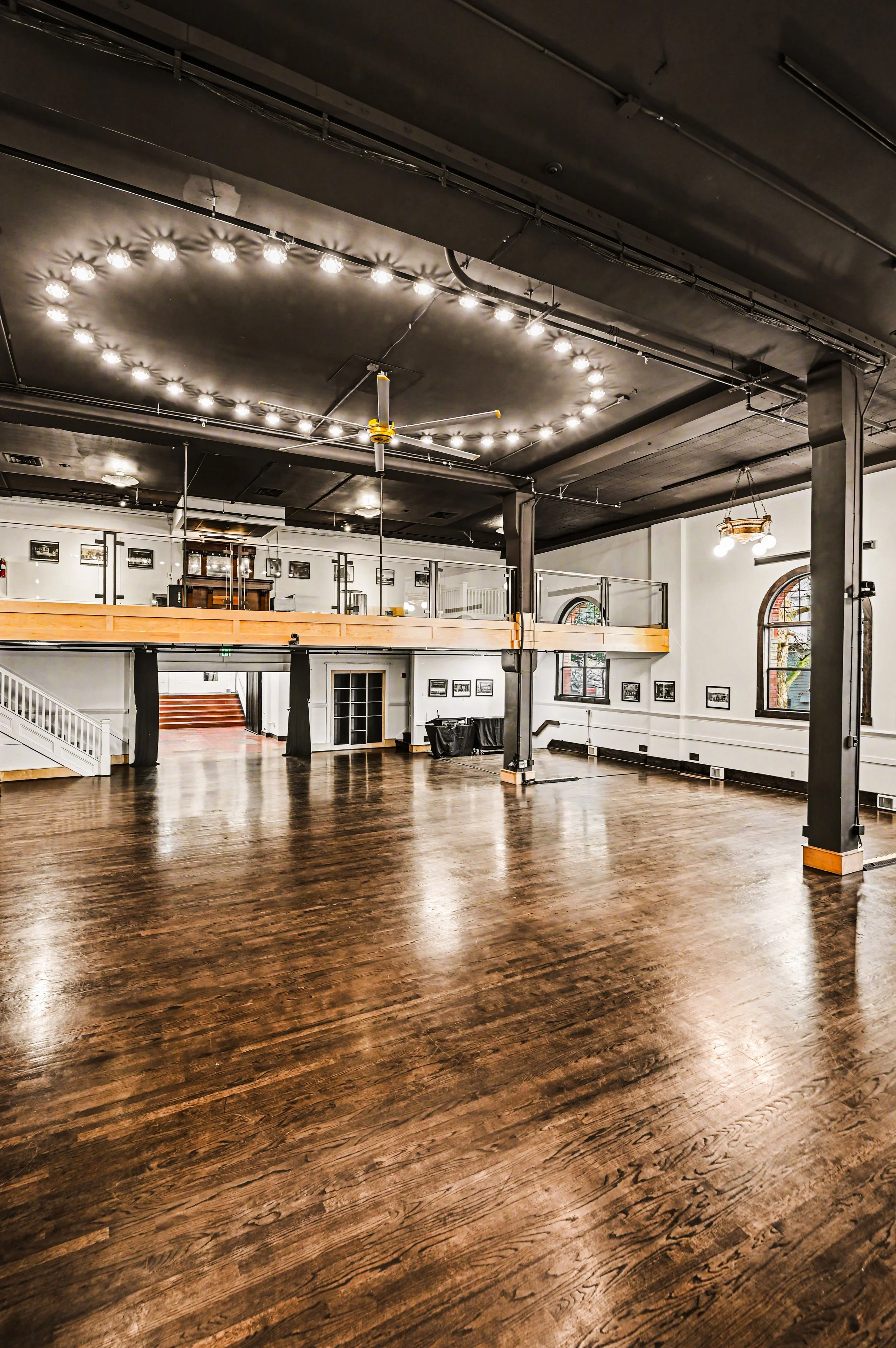Nippon kan theatre, seattle, washington, event space, wedding,Empty dancing or event hall with wooden floors, high ceilings, hanging light fixtures, and a balcony with framed photos on white walls.