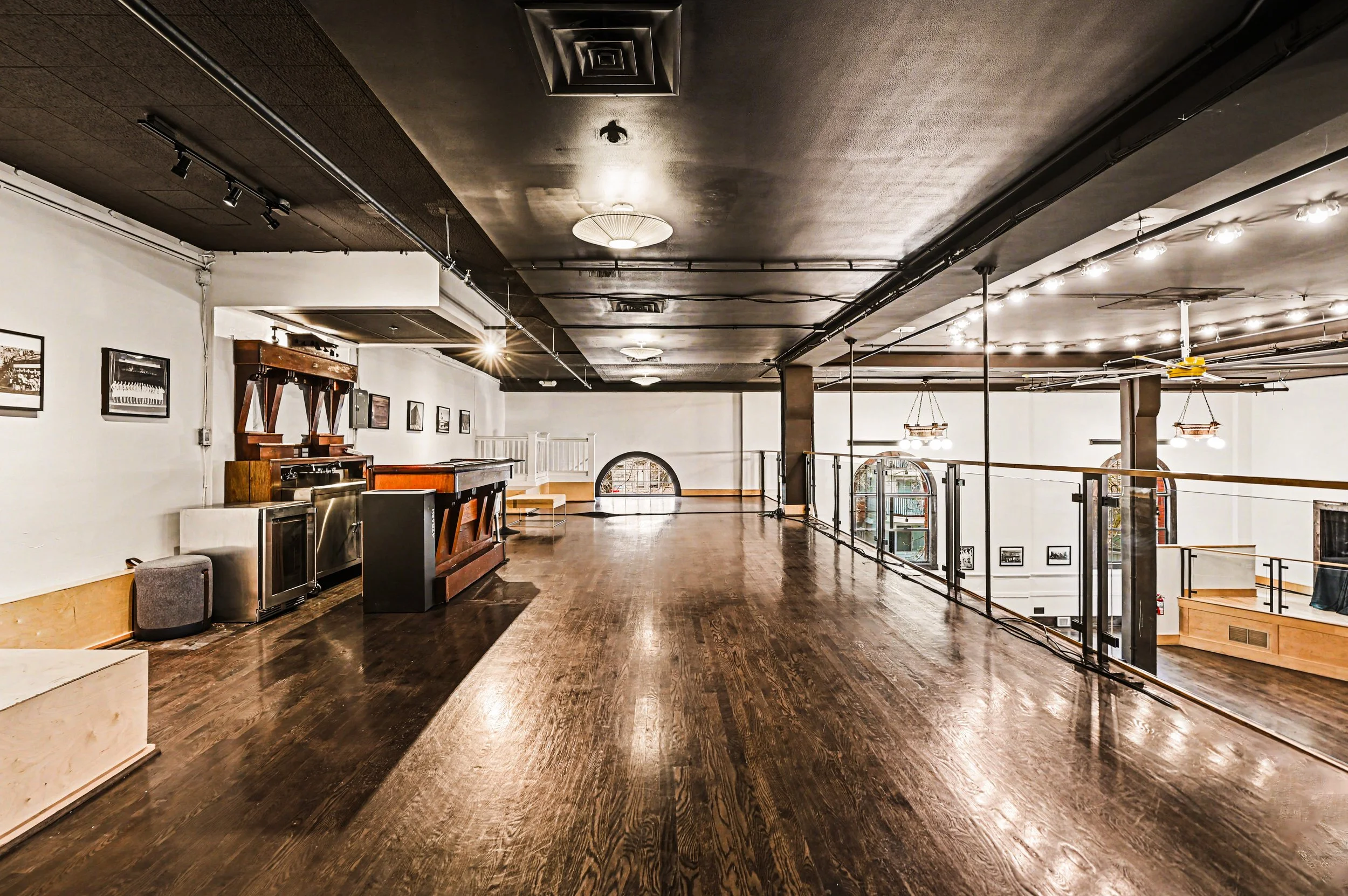 Nippon kan theatre, seattle, washington, event space, wedding,Empty interior space with dark hardwood floors, white walls, and ceiling with lighting fixtures, featuring a bar area and staircase, with arched windows and black railings.