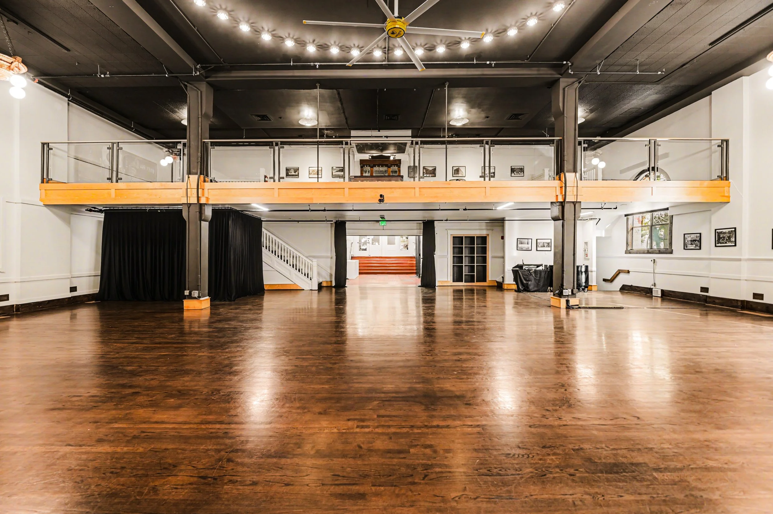 Nippon kan theatre, seattle, washington, event space, wedding,Empty dance studio with wooden floor, black curtains, stairs, and artwork on white walls, with a mezzanine level and ceiling fan.