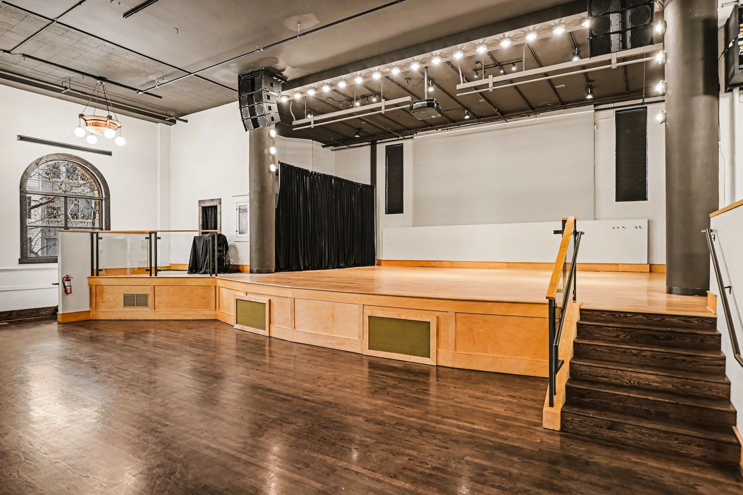 Nippon kan theatre, seattle, washington, event space, wedding,Empty stage with black curtain, wooden flooring, white walls, and windows in a performance venue.