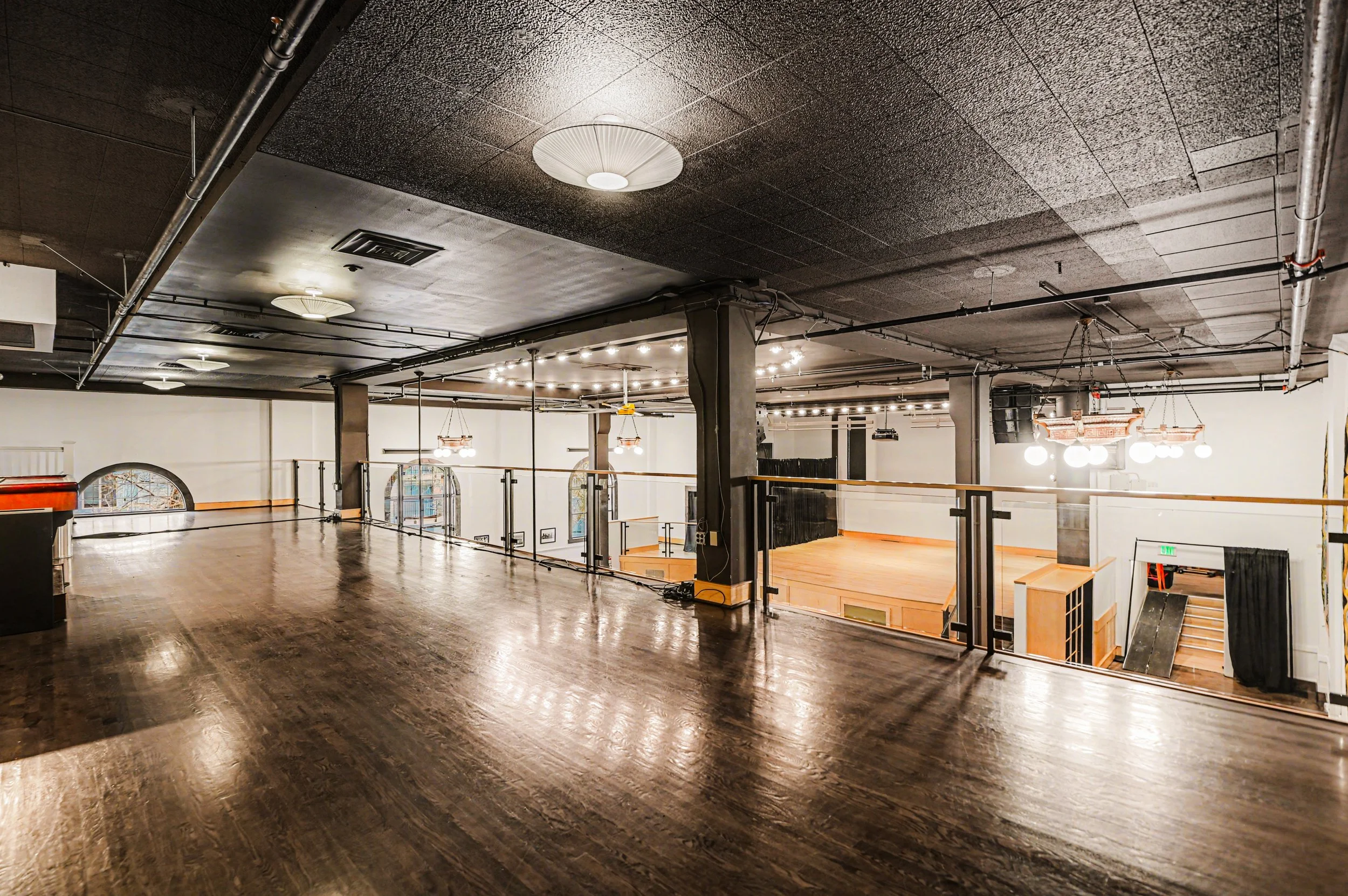 Nippon kan theatre, seattle, washington, event space, wedding,Empty indoor event space with a wooden floor, black ceilings with lights, and a raised stage area with stairs leading down, black curtains, and decorative lighting.