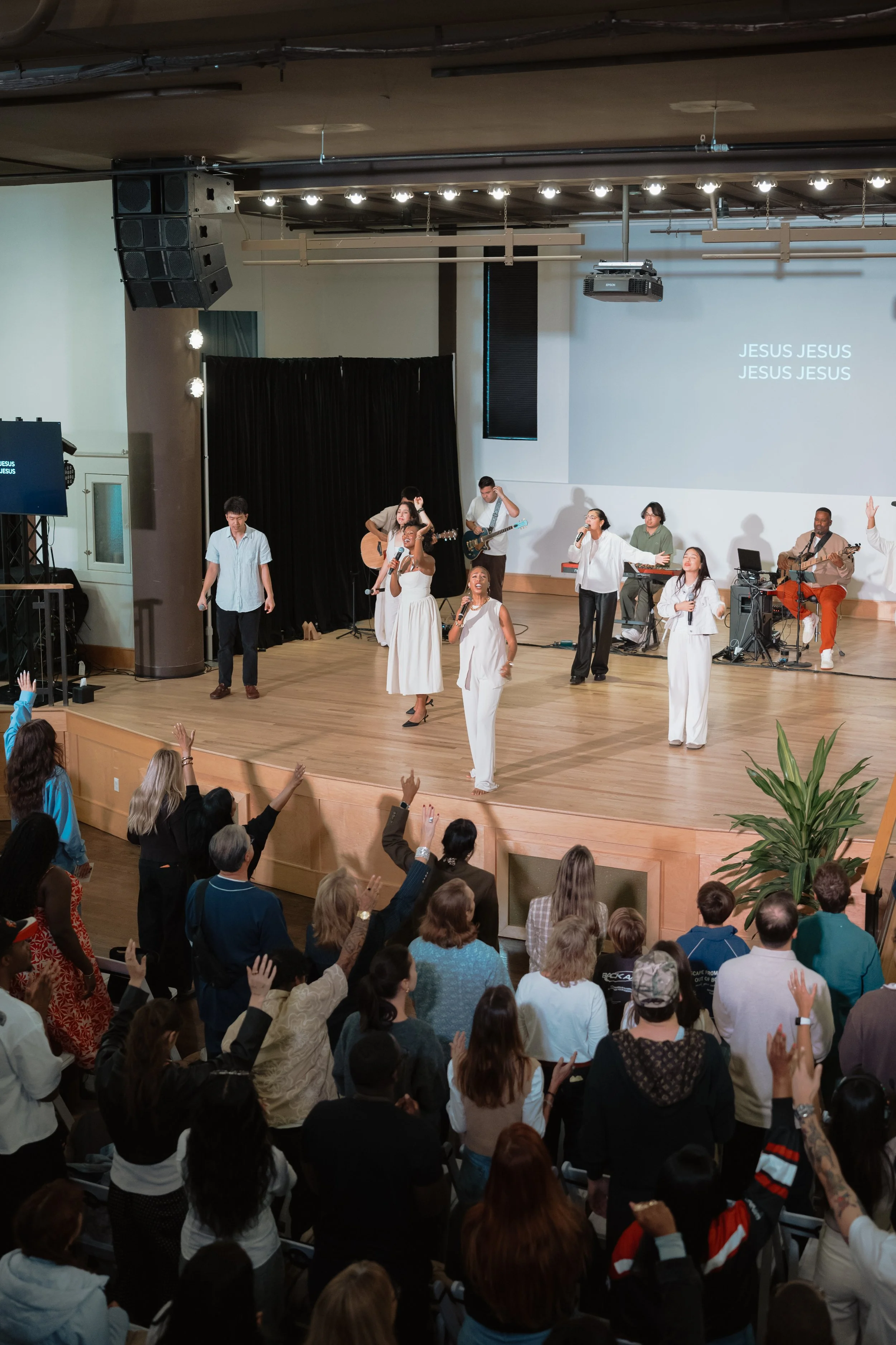 A worship service with musicians and singers on stage and an audience raising their hands in praise.